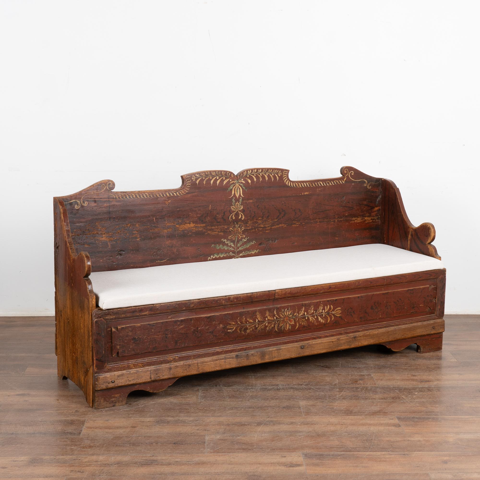 Este original banco de pino sueco pintado a mano muestra un fondo de imitación de madera de color rojo ladrillo/marrón y un sencillo motivo de arte popular a lo largo del panel frontal y el respaldo.
El asiento corrido se abre/se extrae para dejar a