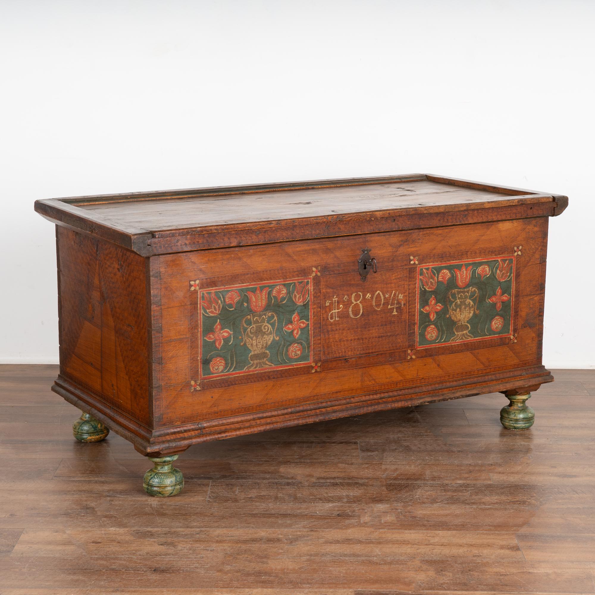 The paint is all original on this delightful flat top trunk from Austria.
The flowers in vases are depicted in the front panels, which was a popular folk art design throughout the 1800's.
The trunk is dated 1804 on the center front and rests on