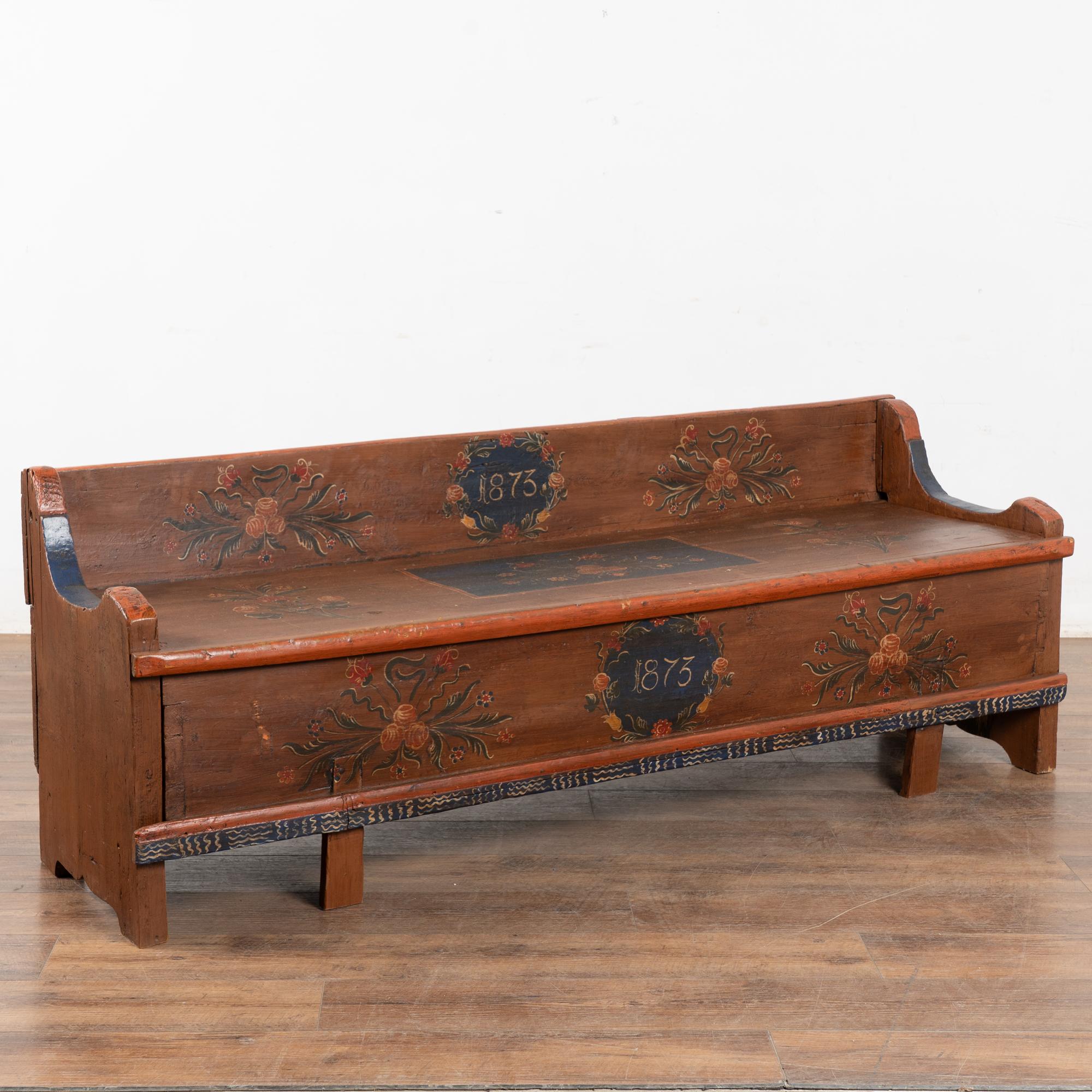 L'antica panca in legno di pino dipinta a mano, datata 1873, è impreziosita da una pittura folkloristica tradizionale dell'Europa orientale con accenti blu e bouquet di fiori rossi su uno sfondo marrone.
Il sedile a panchina si apre per rivelare il