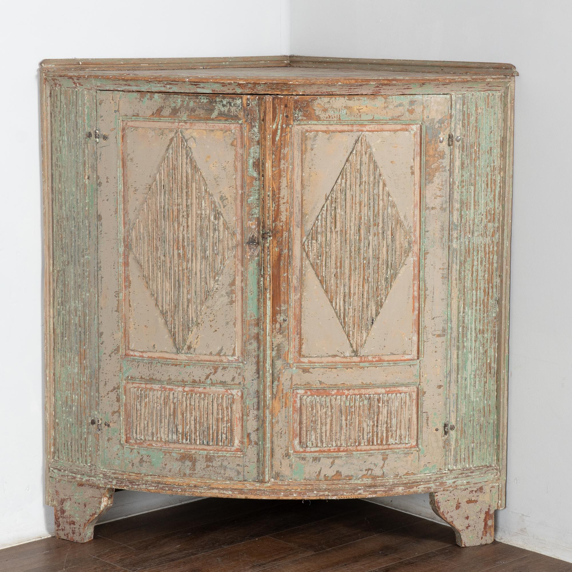 Low corner cabinet from Sweden with original painted finish scraped to reveal layers of green, brick red and white as well as the natural pine below resulting in attractive, warm patina. 
Traditional fluted diamond motif on panel doors, with