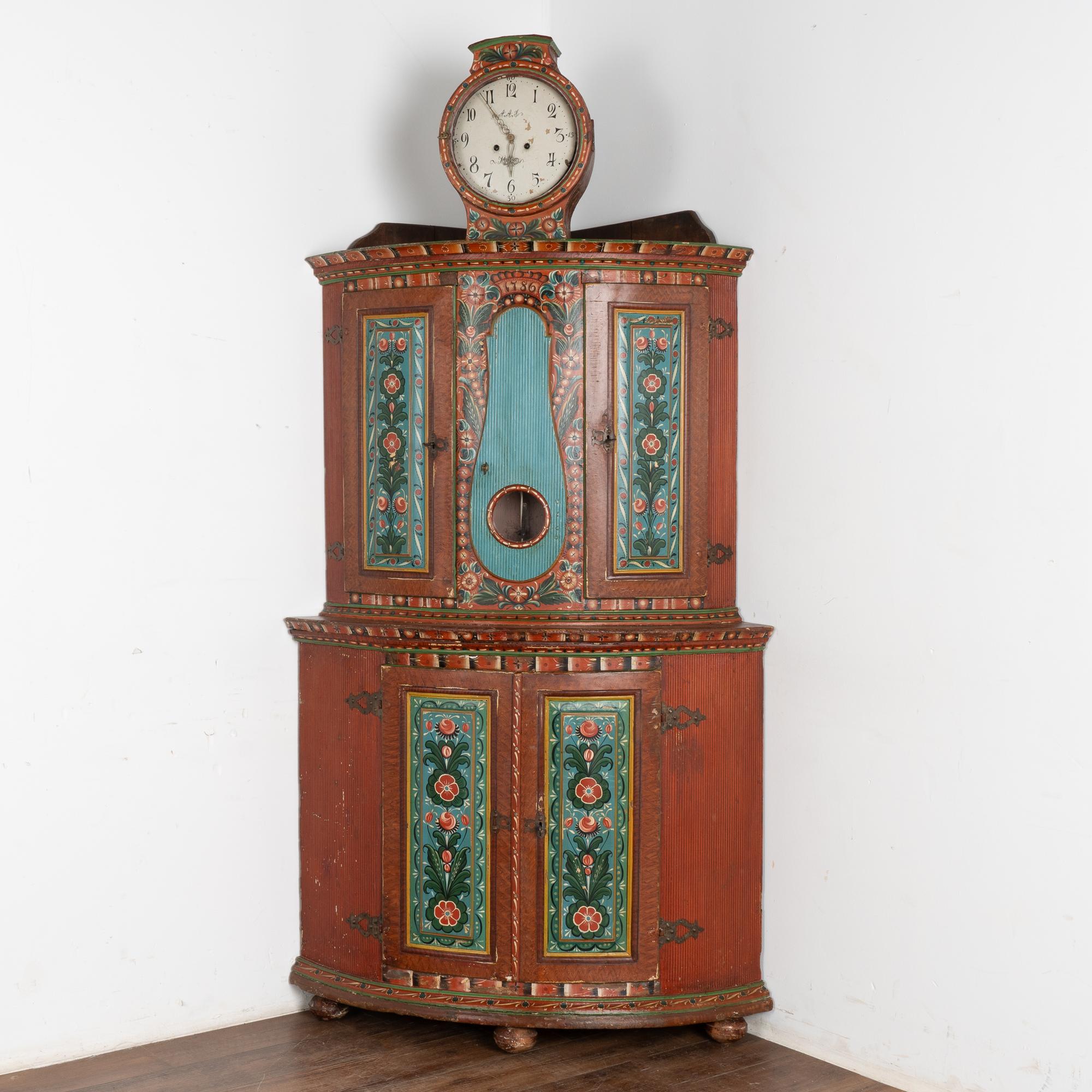 Questo mobile angolare in pino con fronte ad arco include un orologio svedese Mora Clocks incorporato, il che lo rende un reperto speciale.
La finitura originale verniciata presenta segni di usura e di deterioramento legati all'età, compreso lo