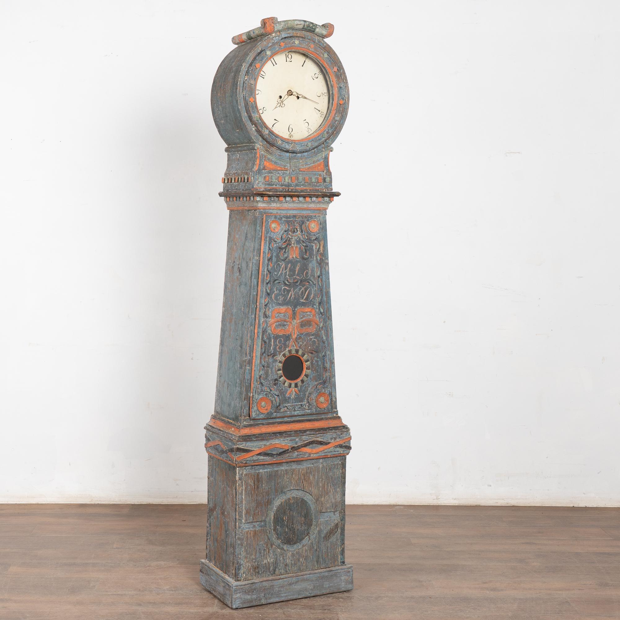 Original 19th-century Swedish Mora clock dated 1823, crafted from pine with its original blue and faded red painted finish. Exceptional carved details include fluted base, ribbon, tulip, diamonds, and dentil molding. Distressed surface reveals