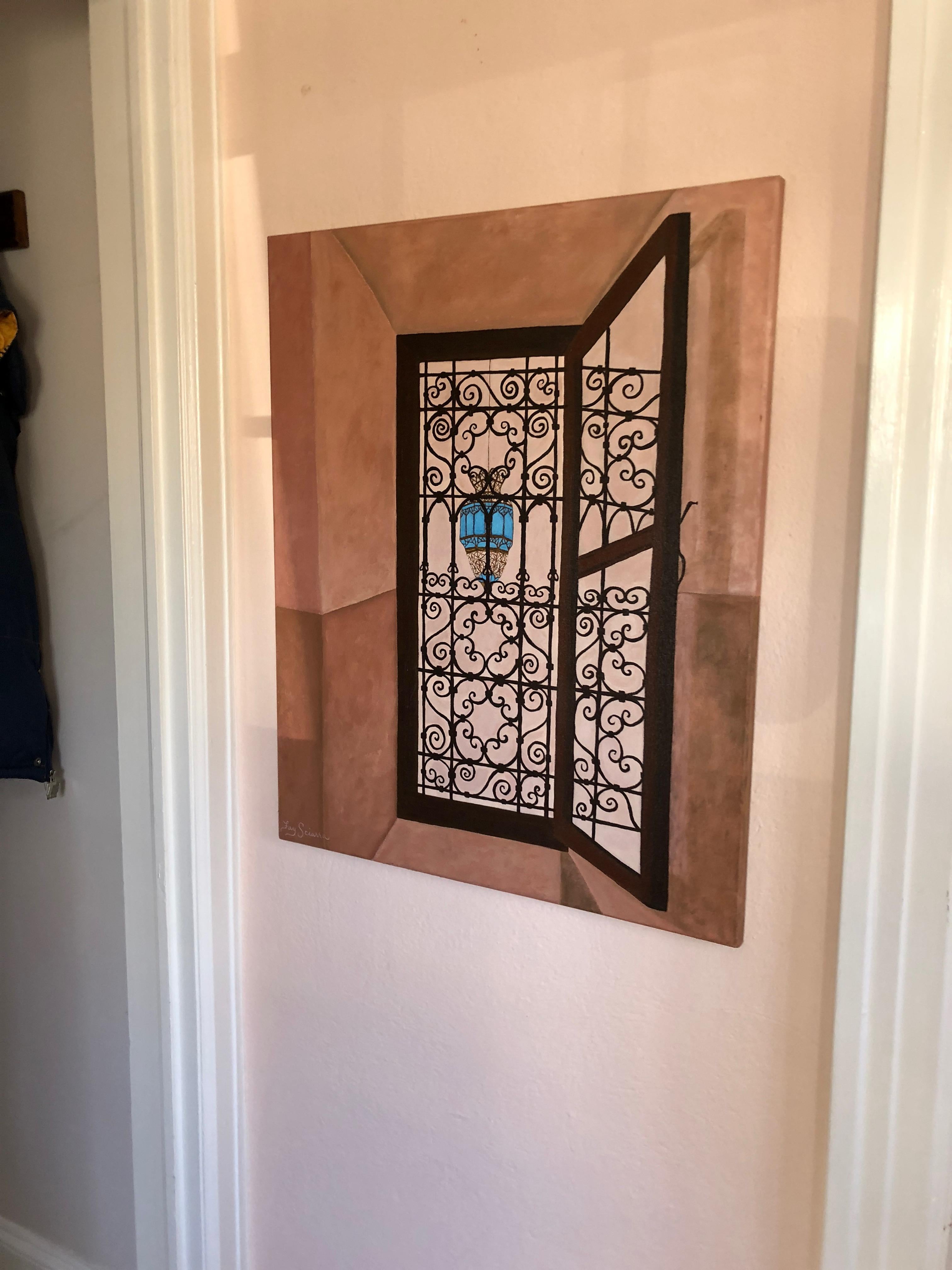 A stunning original painting on canvas inspired by a narrow rectangular window in a stucco Moroccan riad having meticulous curliecue designs on an iron grill. View through the opening is of a typical Morrocan style light pendant. Color palette is an