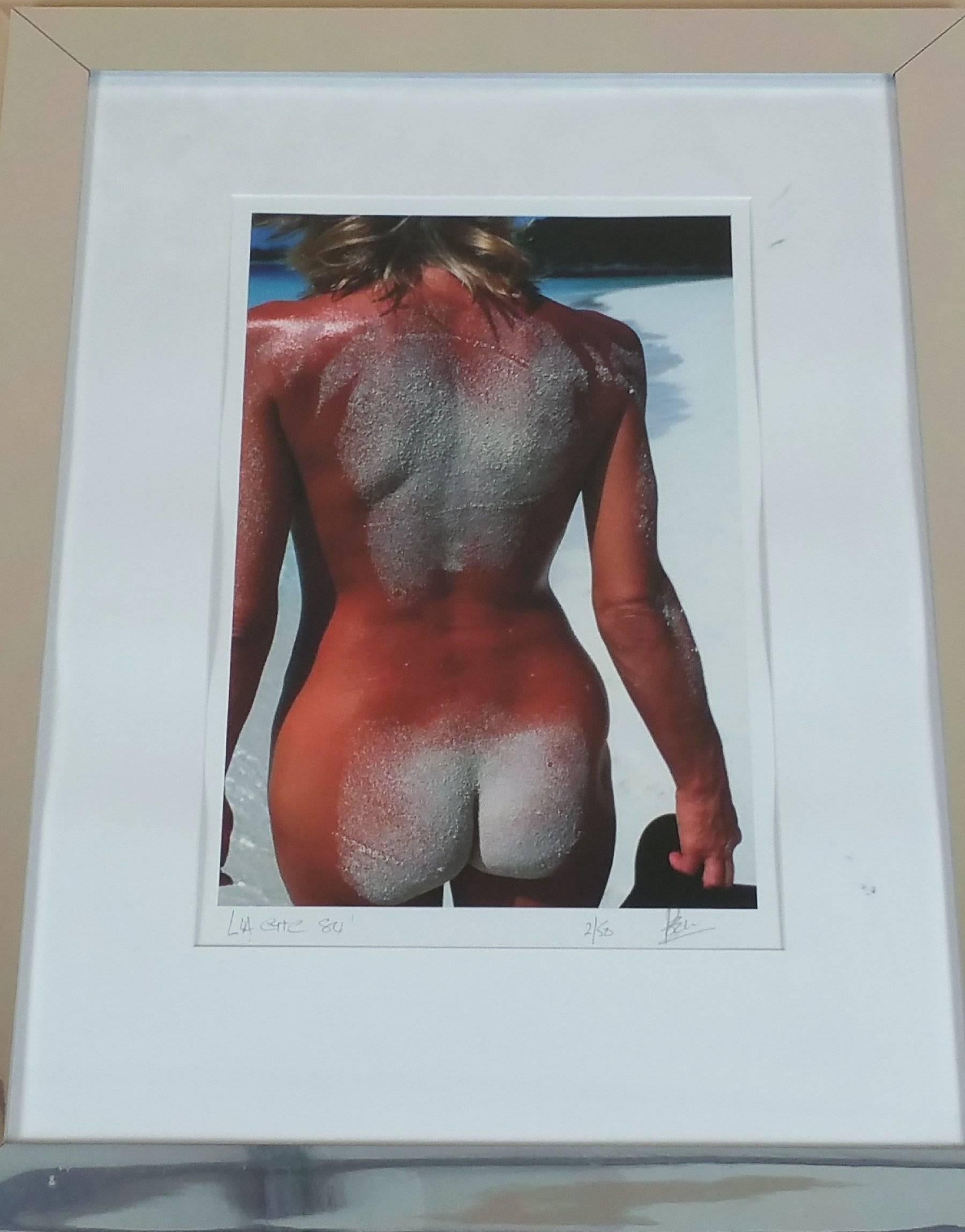 One of two original photographs signed and dated by the artist, which is ‘Poole’, dated 1984. The color photograph depicts the back of a nude woman walking on a beach, possibly on the west coast of the United States. The picture measures 28 ½ inches