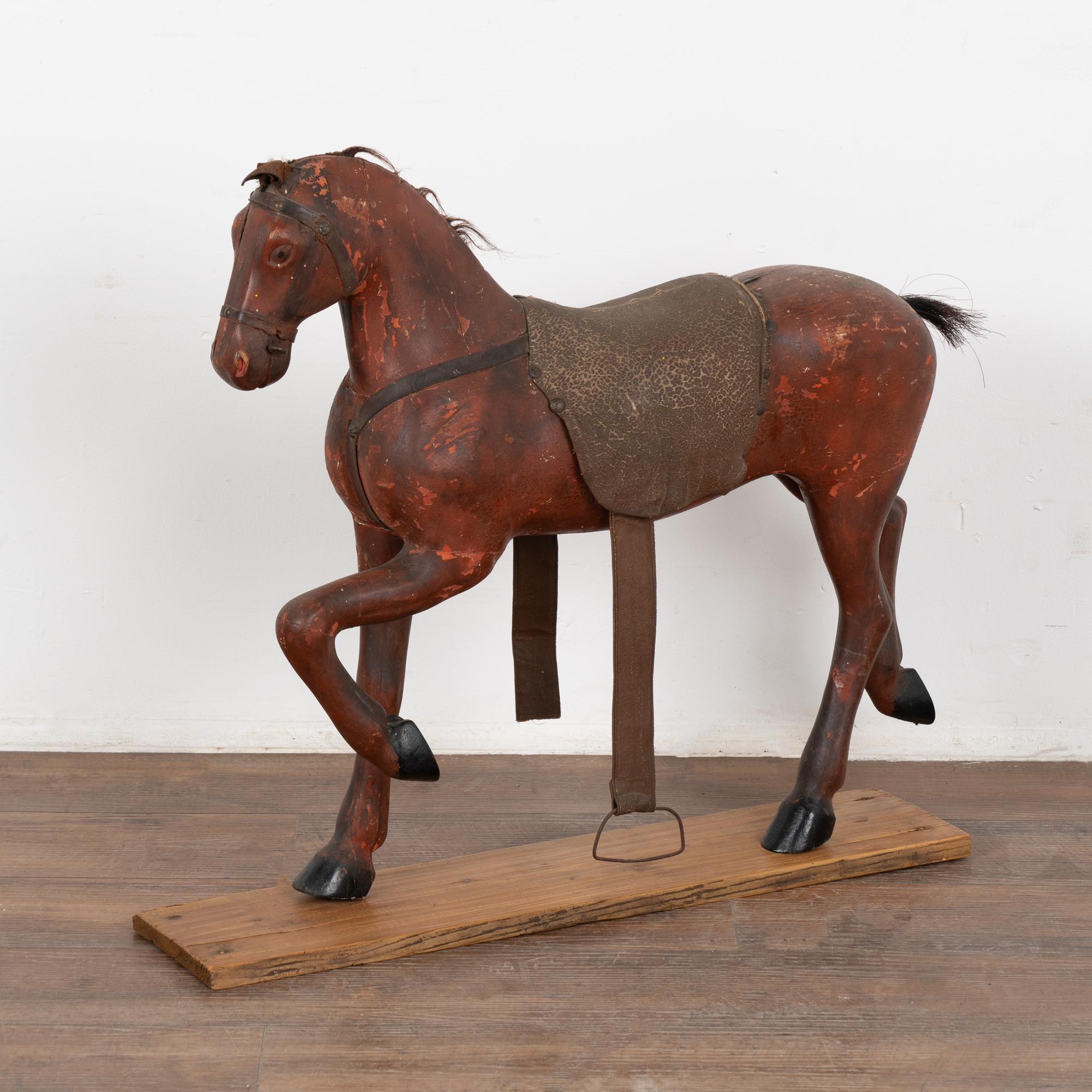 It is the very worn look that creates the wonderful appeal of this original painted and carved horse from Sweden. 
The brick red paint has been chipped and distressed while the tattered leather ears, parts missing to bridle and crackles to the old
