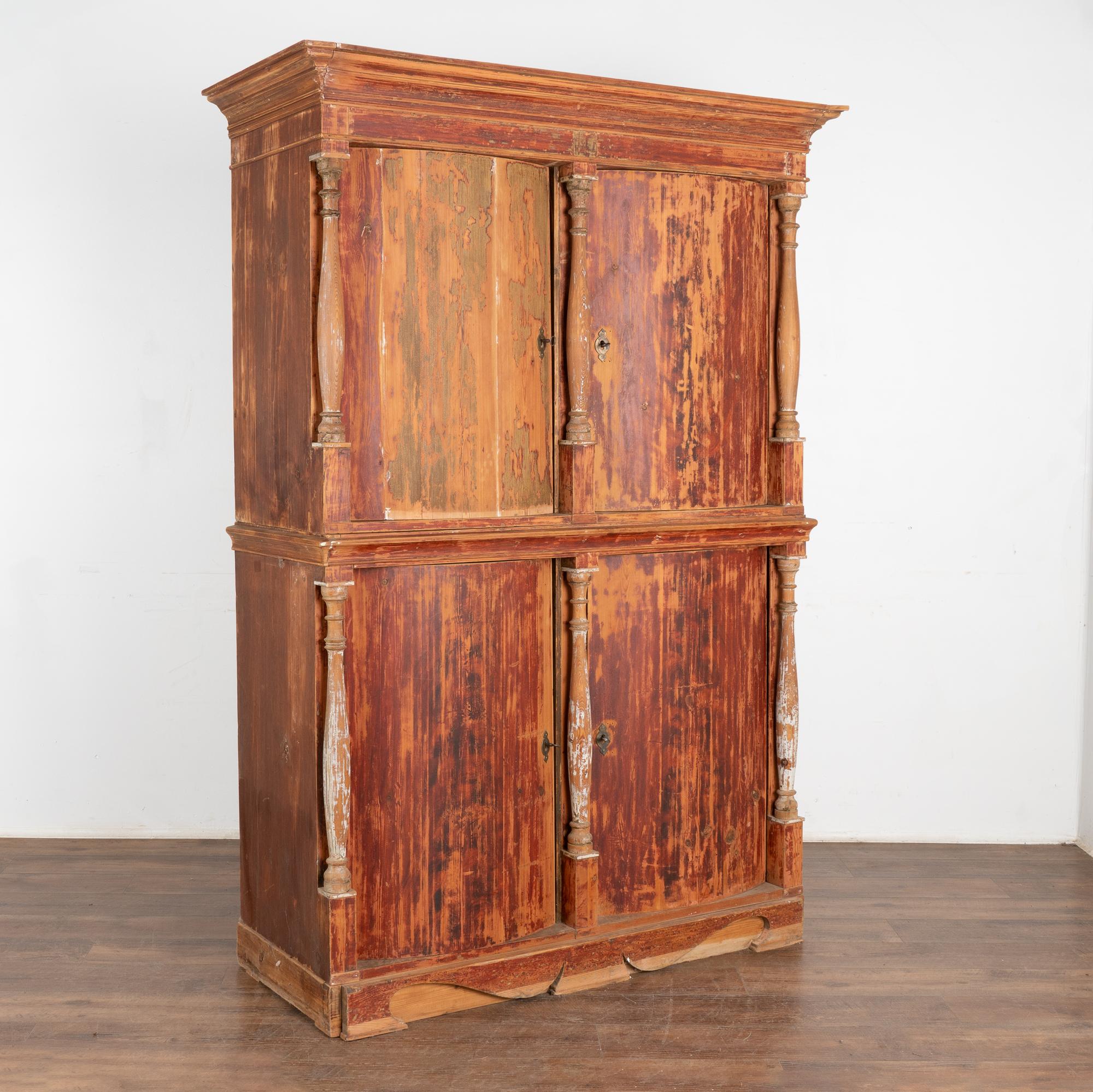 The great appeal of this remarkable four door cabinet is largely due to the original brick red paint, which has been scraped leaving a soft, raw feel to the finish. The six turned columns were originally painted white, now providing a faint and