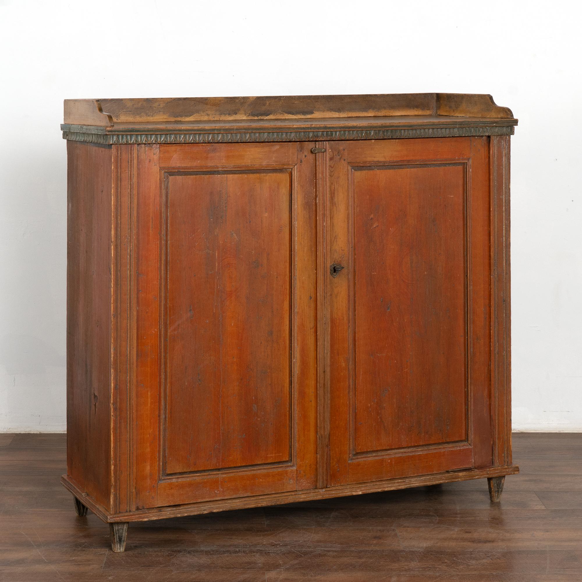 This pine sideboard is a wonderful example of Swedish country craftsmanship with a warm, aged patina in the original brick red painted finish and contrasting green/teal paint along the carved upper trim. 
Two doors open to reveal three interior