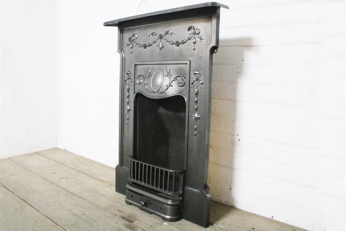 Original restored antique classical Edwardian bedroom fireplace decorated with ribbons and bell flowers. 

Finished with traditional black grate polish and complete with a new clay fire back and cast iron bottom grate ready for a solid fuel fire.