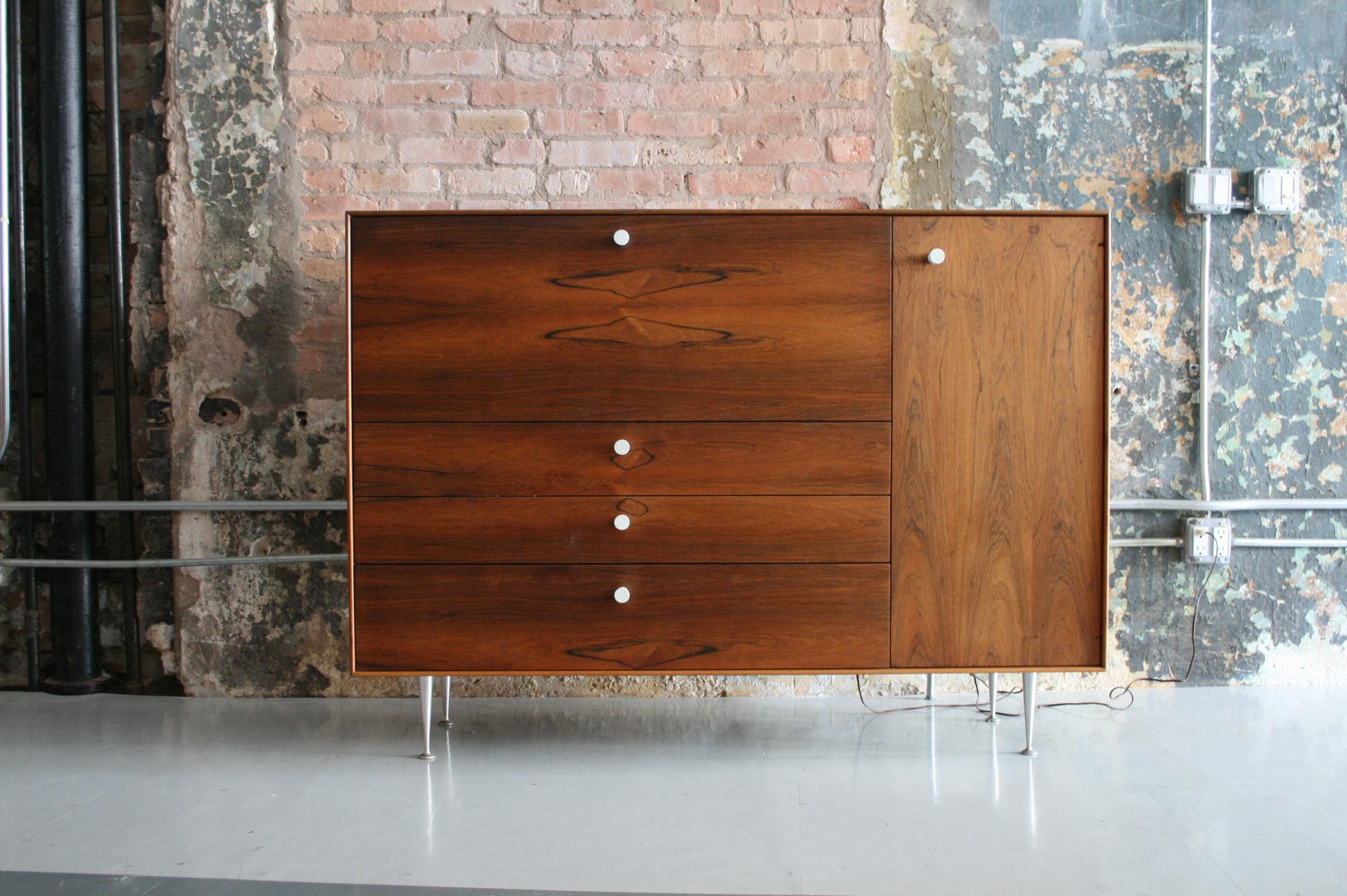 This is a Thin Edge Series secretary cabinet / desk designed by George Nelson for Herman Miller. Named for its clean lines, the minimal Rosewood case floats on aluminum champagne flute legs and finished with Nelson's signature porcelain knobs. Panel