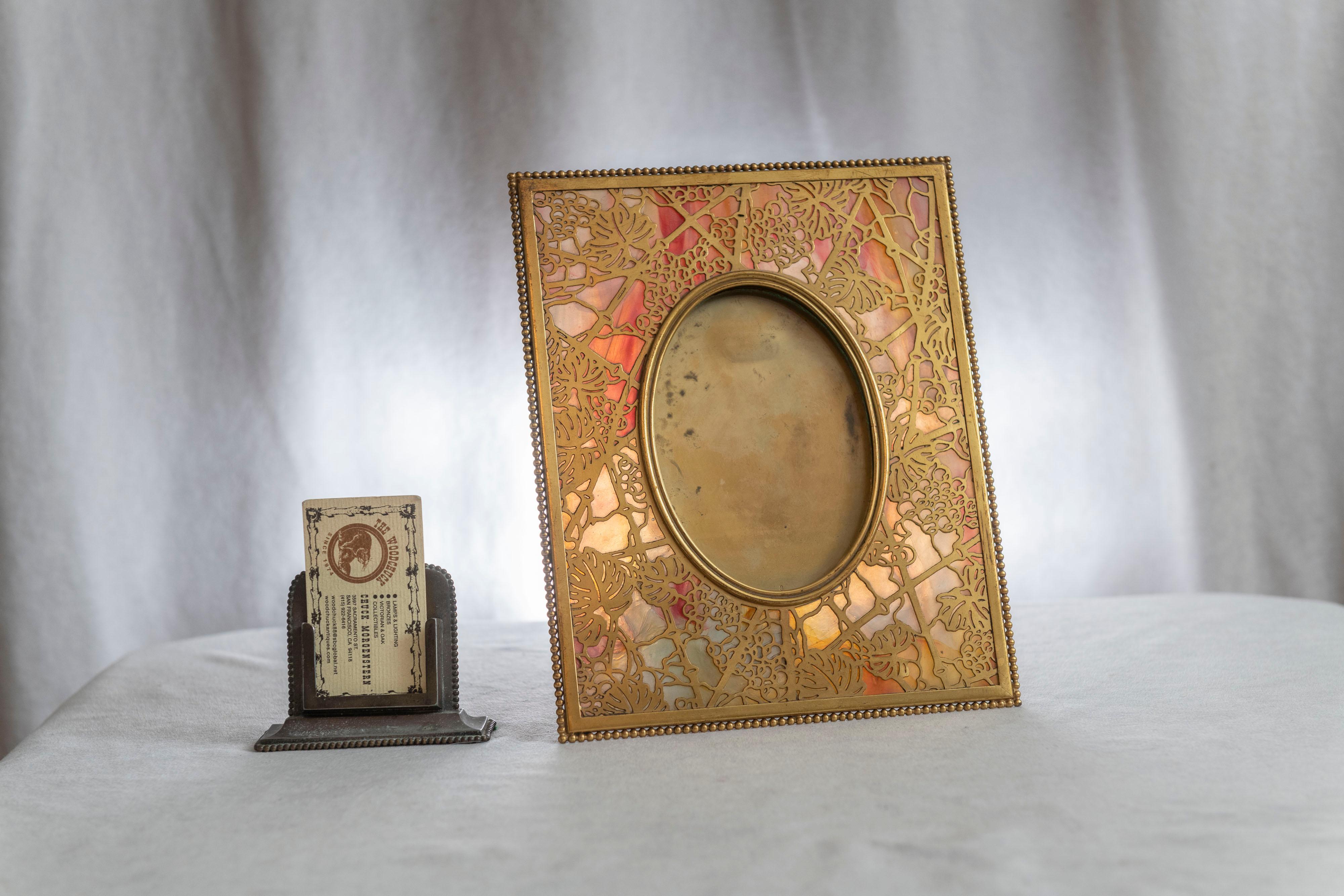 A very fine example of Tiffany Studios workmanship in producing a rich quality picture frame. Using colorful glass as a backdrop and covered in a gilt bronze overlay grapevine pattern. Properly signed on the back and in fine condition.