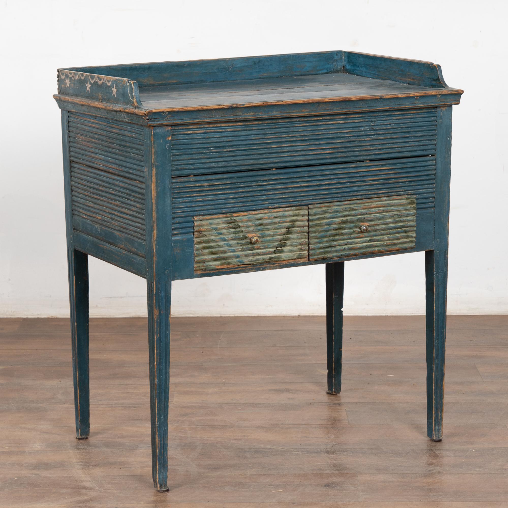 Dieser reizende Beistelltisch aus Kiefernholz stammt aus Schweden und hat noch die ursprüngliche blaue Lackierung mit Monogramm und Datum von 1850 in Weiß.
Außergewöhnliche kannelierte Details an den Seiten, der Vorderseite und den Schubladen in