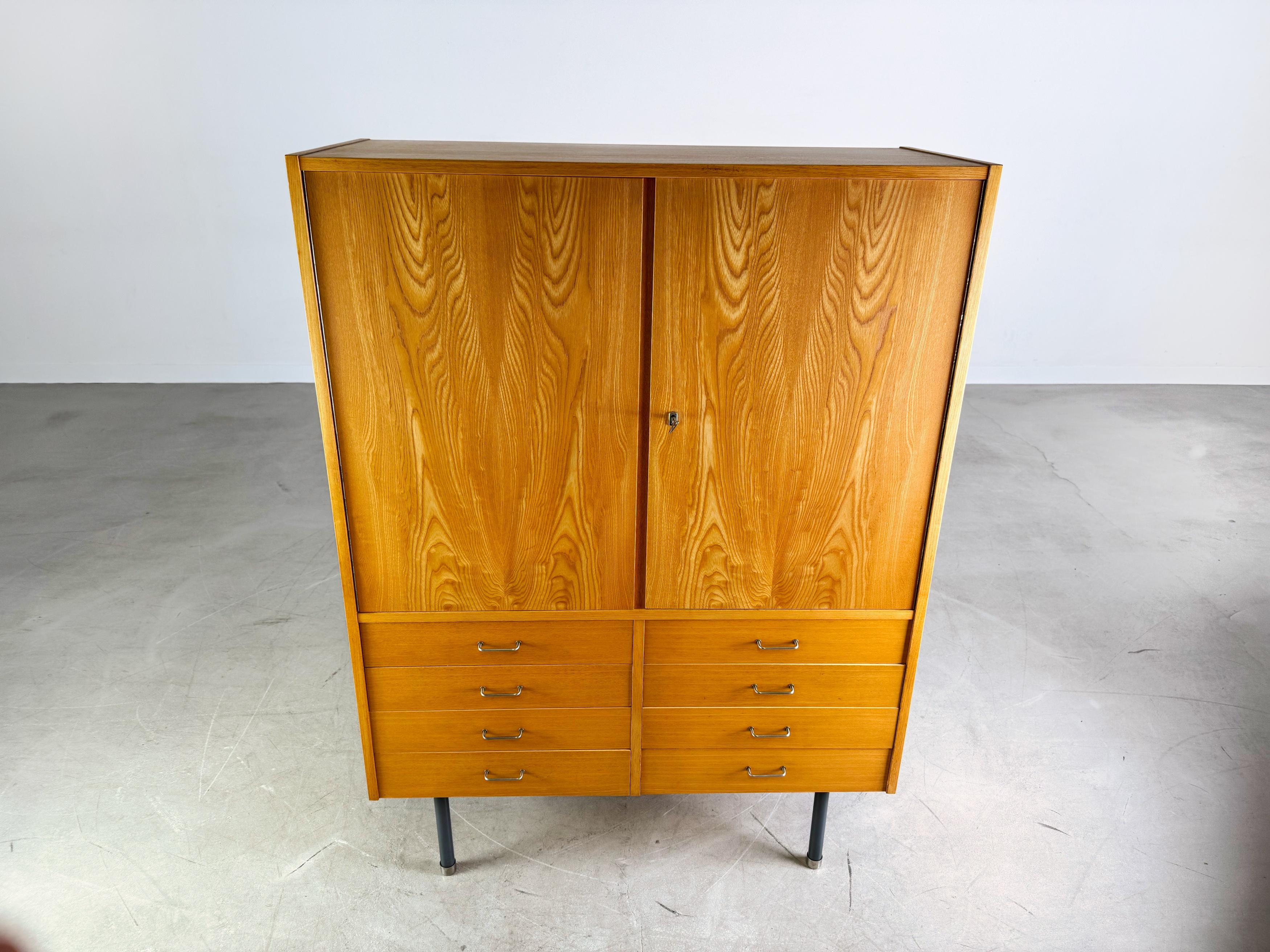 Wir bieten einen wunderschönen Vintage (Hoch-/ Wäsche-) Schrank aus den 1960er Jahren zum Verkauf an. Das Möbel wurde vom renommierten deutschen Hersteller VEB DW Hellerau hergestellt und bietet mit acht Schubläden und zwei Türen ein großes