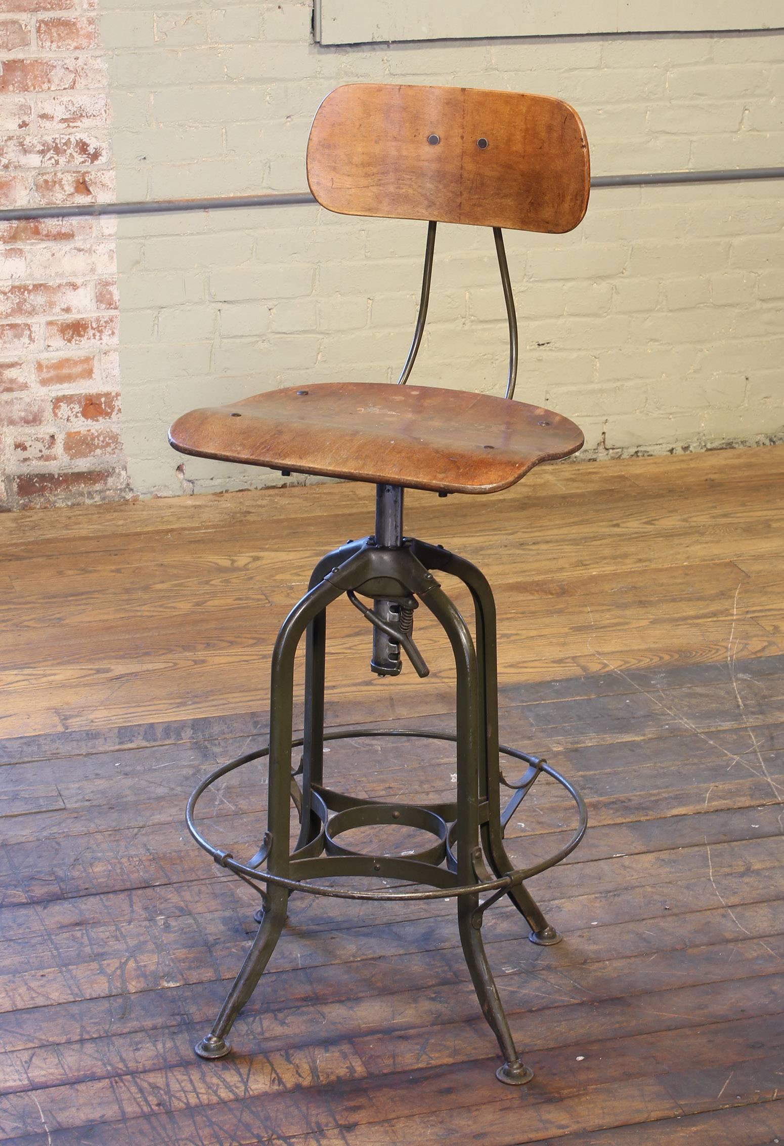Authentic original adjustable Toledo bar stool. Bent plywood seat and back, distressed military green painted steel frame. Seat ring diameter measures 18