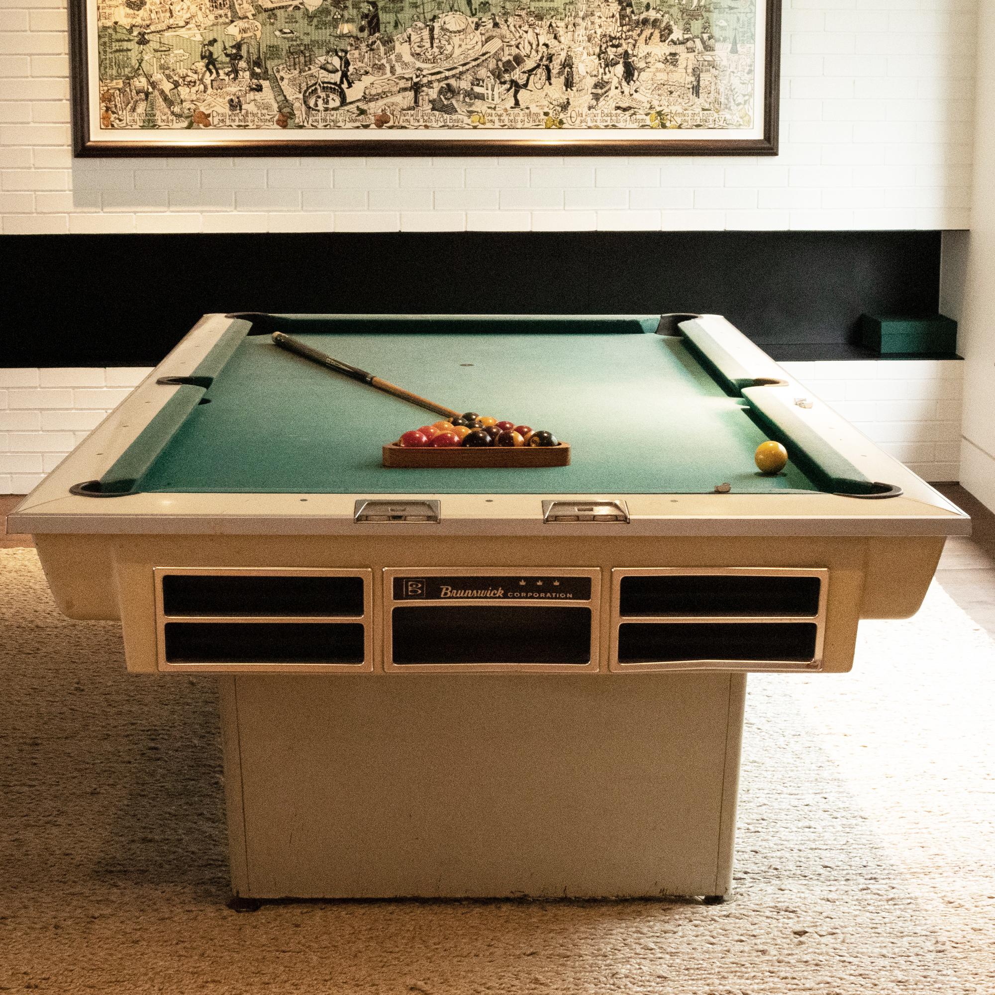 This 1960s original American pool table by Brunswick is a fantastic vintage piece.
The off-white frame sits on angled wooden legs and features a silver metal trim and green cloth.
The pool table has two dials at one end to keep score and comes