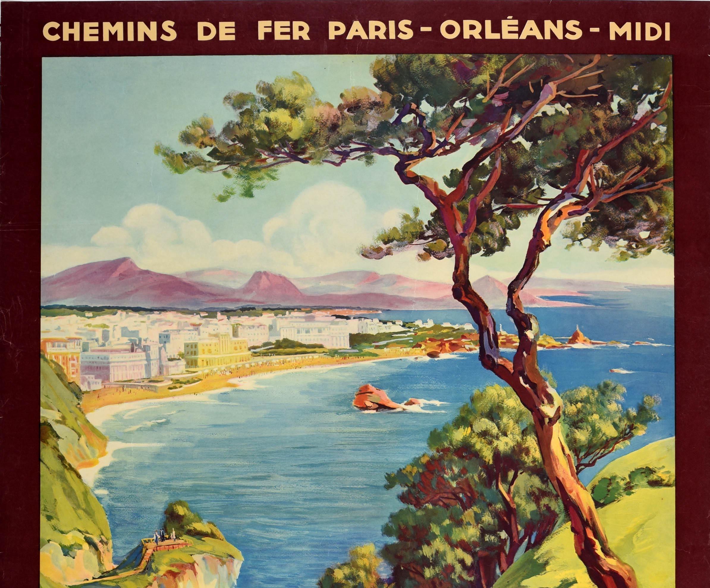 Original vintage railway travel poster for Biarritz featuring a scenic view over the coast depicting a couple walking down the path by flowers and trees in the foreground, the rocky cliffs leading round to people on a sandy beach and swimming in the