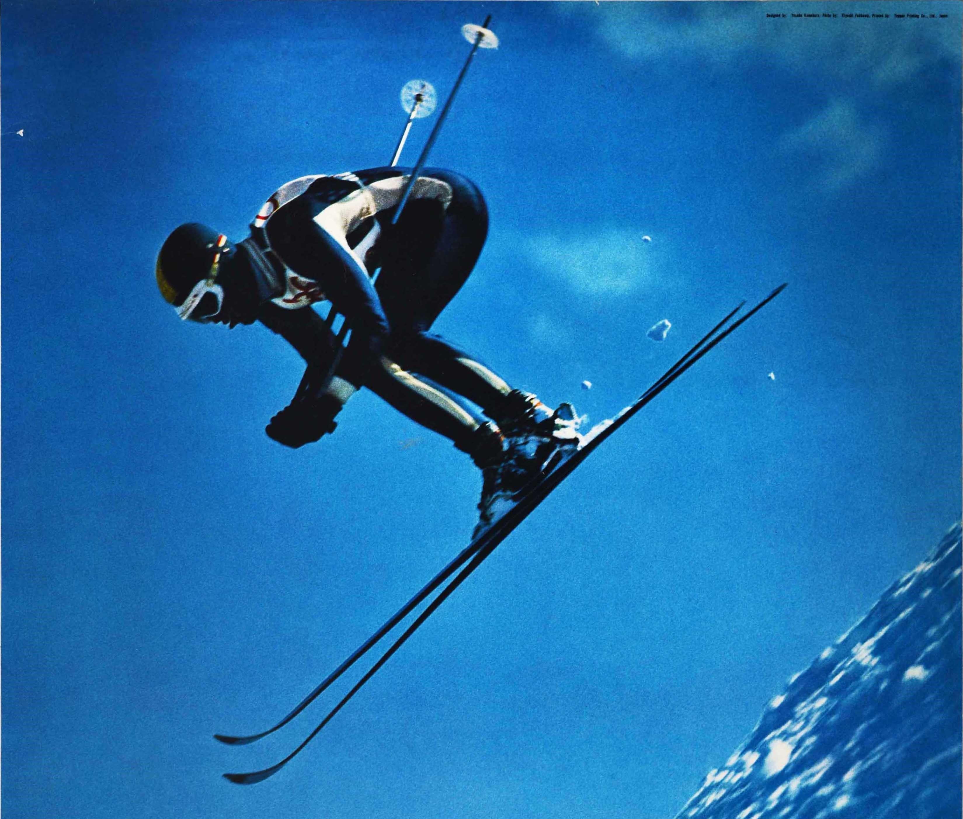 Original-Sportplakat für die XI. Olympischen Winterspiele, die vom 3. bis 13. Februar 1972 in Sapporo, Japan, stattfanden. Es zeigt einen Skifahrer, der mit hoher Geschwindigkeit über eine verschneite Piste springt, vor einem strahlend blauen Himmel