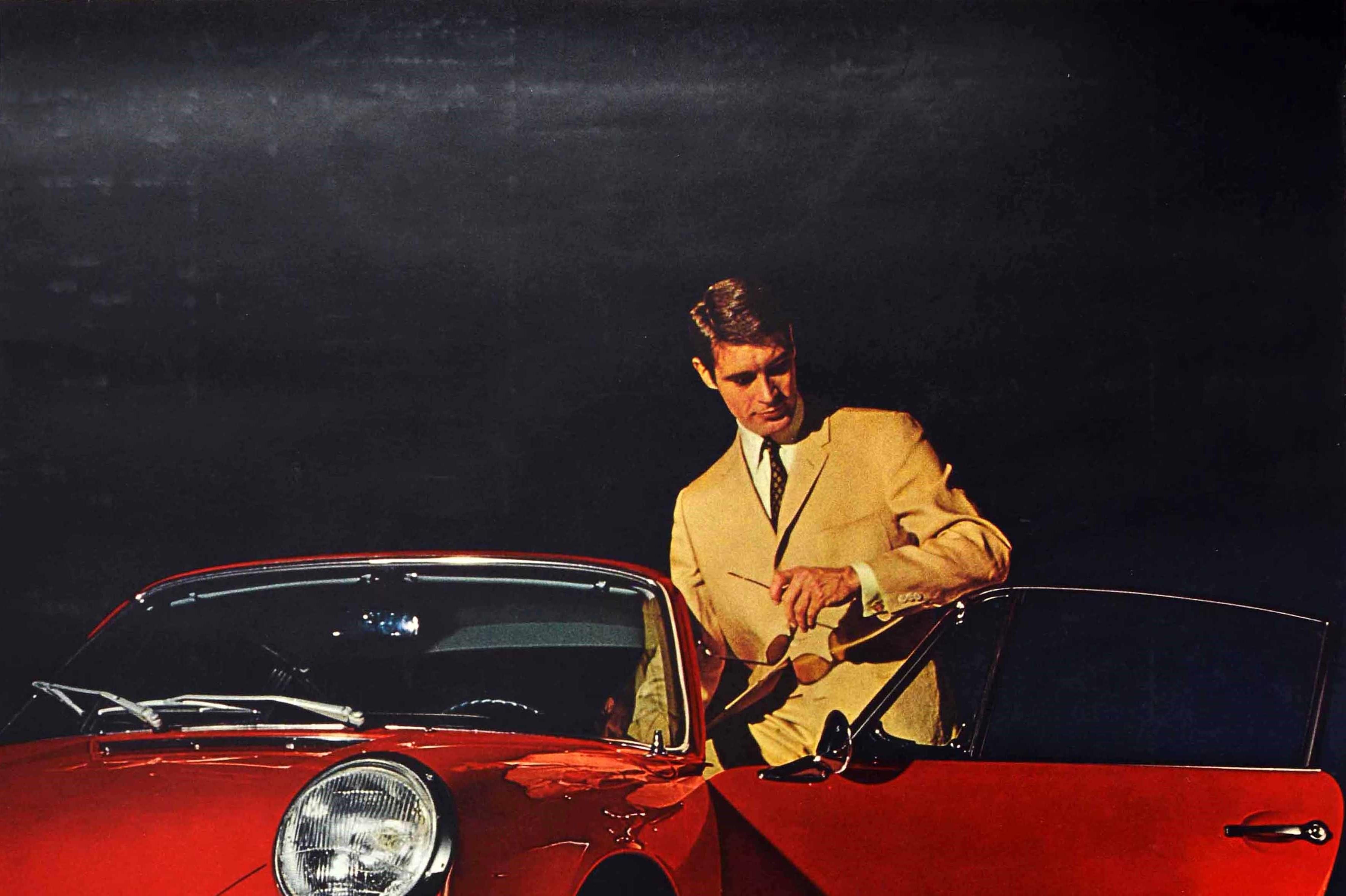 Original vintage car advertising poster for Porsche 911S featuring a photograph of a young man in a beige suit and holding sunglasses in his hand standing at the open door of a shiny new red Porsche 911S against a black background with the bold blue