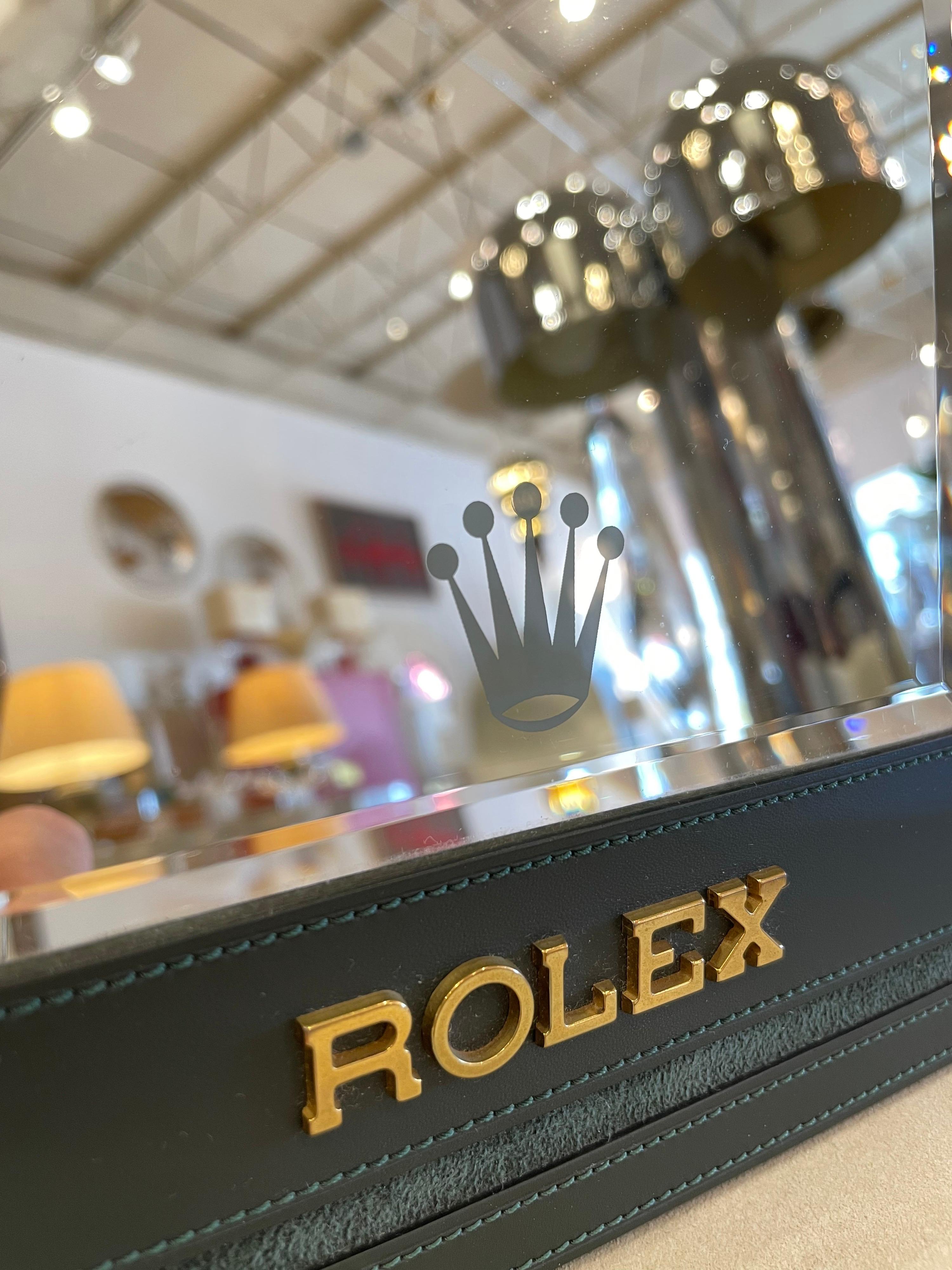 This amazing green stitched leather and suede bound Rolex display mirror features raised brass/gold iconic Rolex Logo on the leather as well as a frosted Rolex crown logo to mirror. Mounted with a beveled edge mirror and on an easel support.