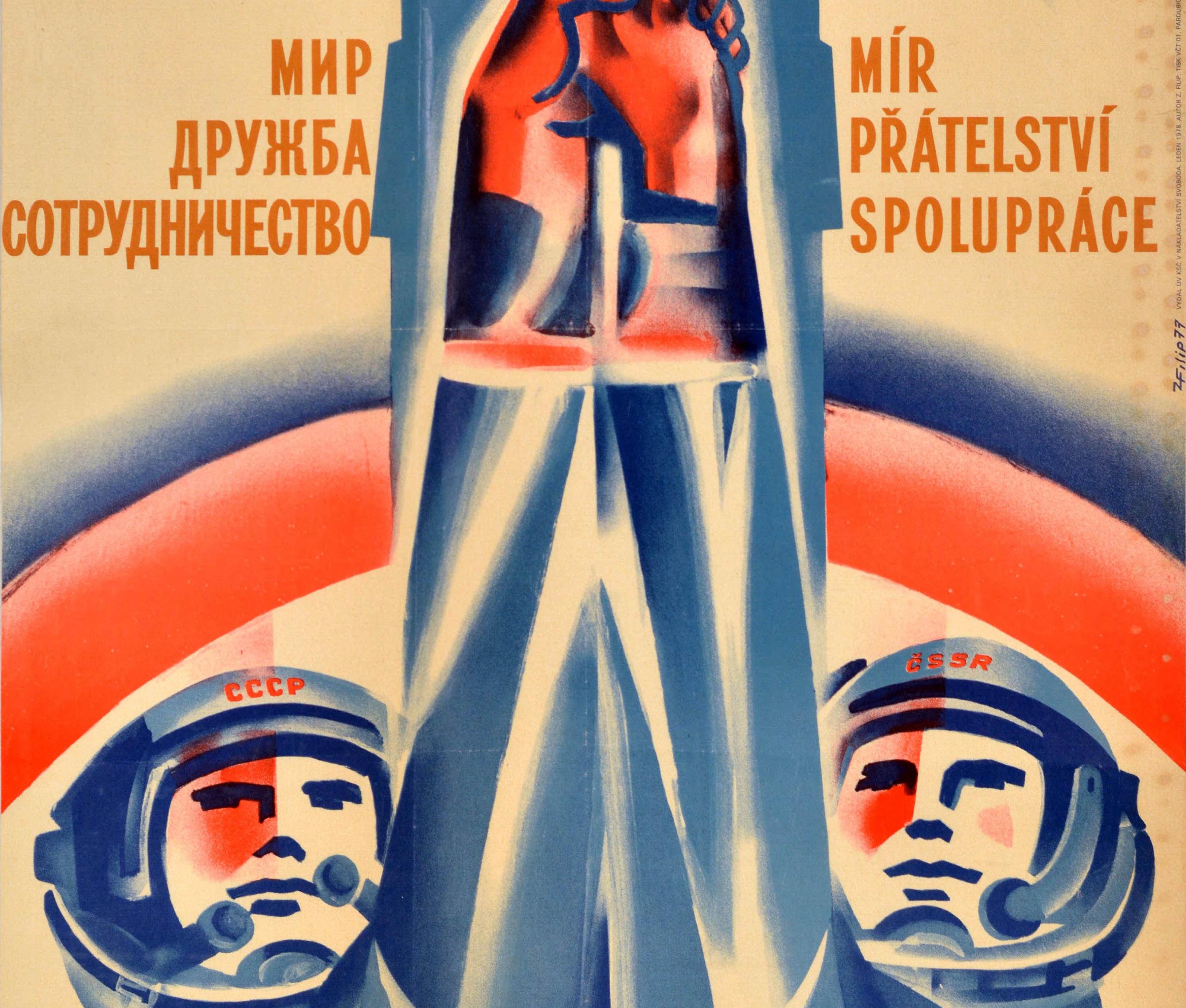 Original vintage Soviet propaganda poster featuring an illustration of two cosmonauts with USSR and Czech SSR on the helmets of their space suits, holding their hands up together against a rocket in the background with the caption in Russian and