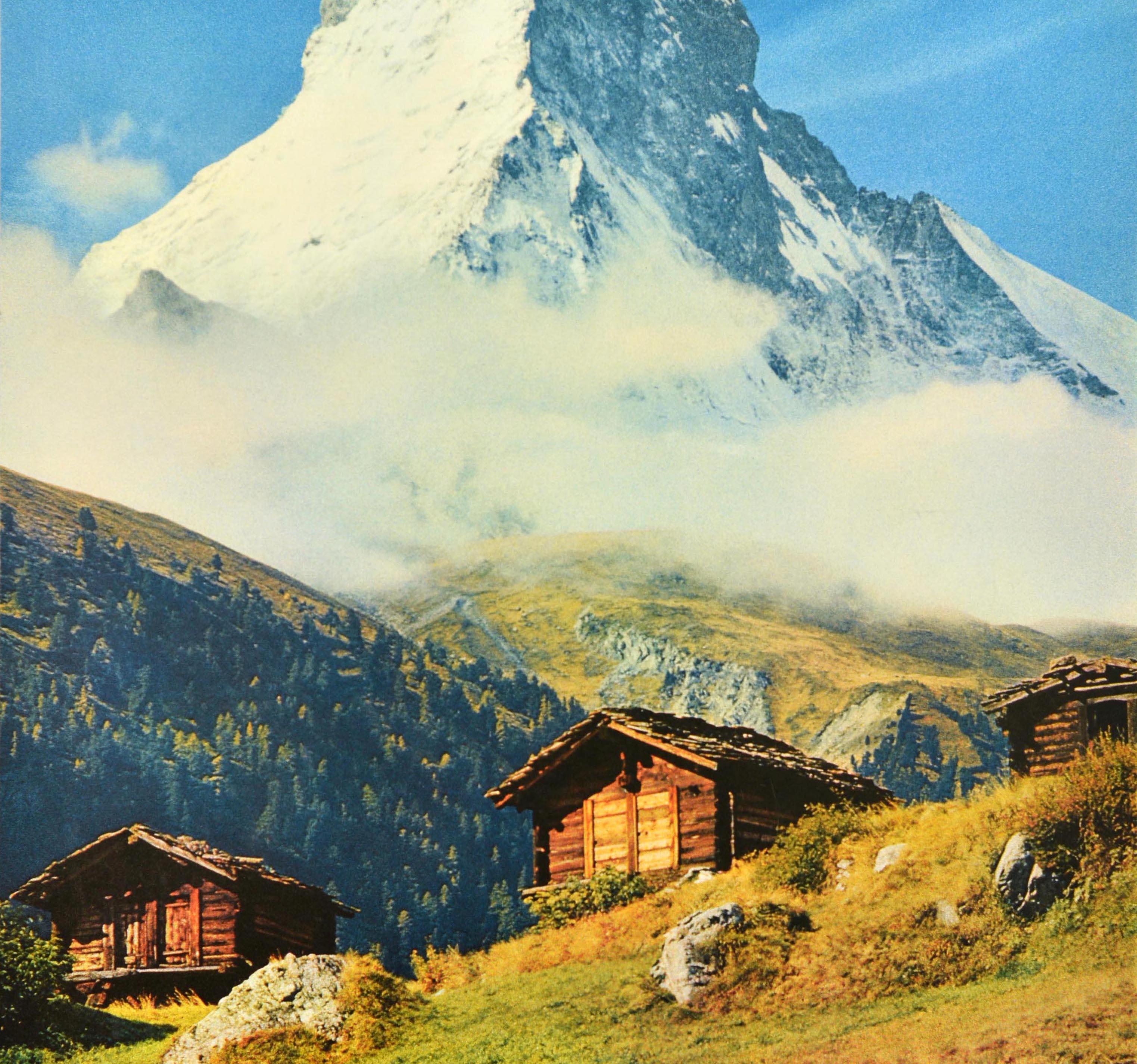 Affiche de voyage originale pour Zermatt Schweiz Suisse présentant une vue pittoresque du Cervin enneigé à travers une fine couche de nuages, en regardant vers le haut des bâtiments traditionnels en bois et des rochers sur un terrain en contrebas.