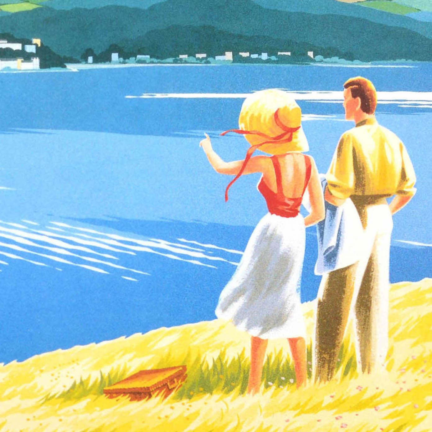 Original vintage travel advertising poster for the Isle of Man featuring a great image of a couple looking at the view from a hill in the foreground, a picnic hamper on the grass, the man holding his jacket over his arm and the lady in a straw hat