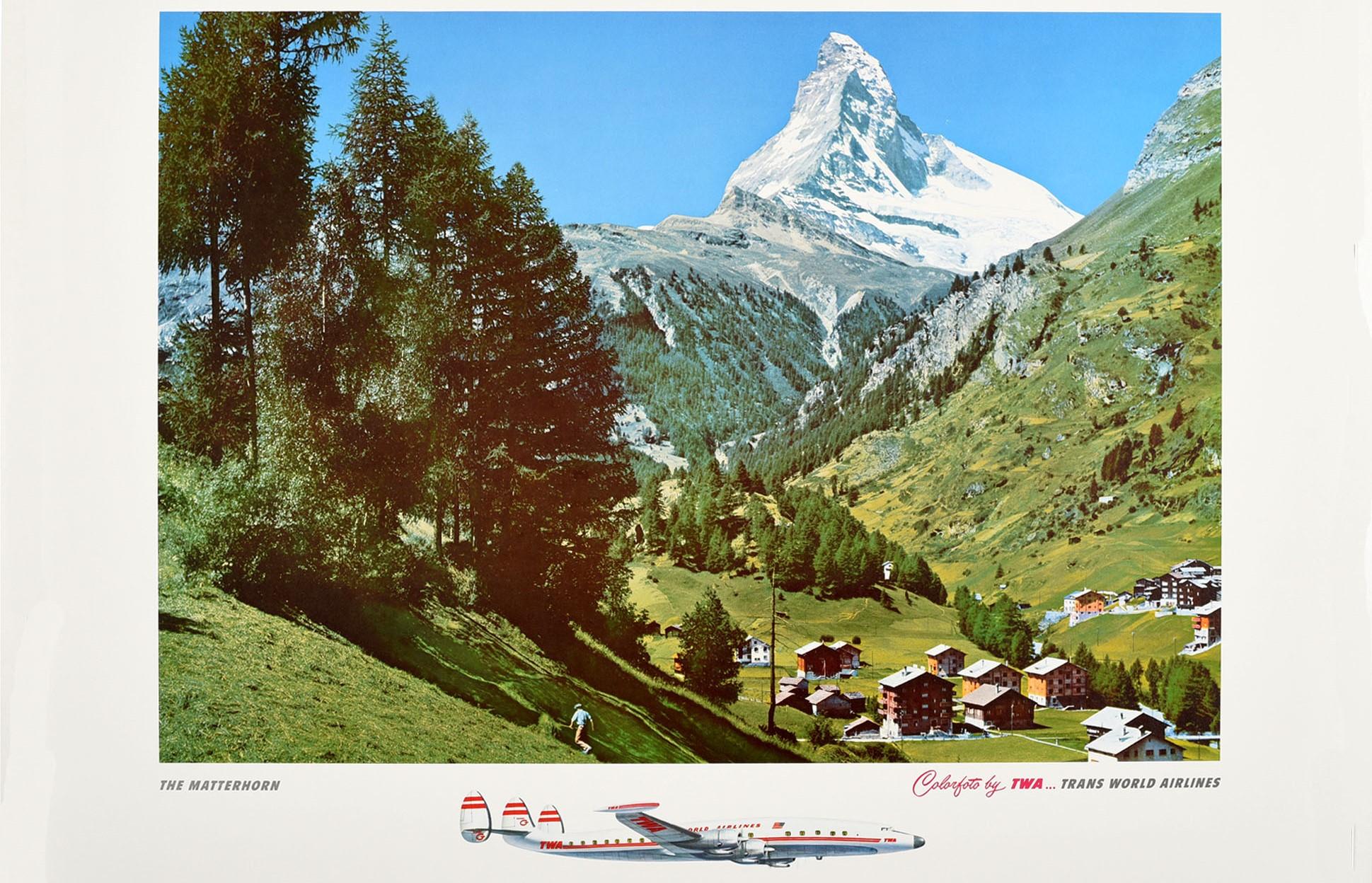 Original vintage airline travel poster - Along the way of TWA... Switzerland The Matterhorn - featuring a colour photograph of trees on a green hill with a small town nestled in the valley overlooked by the snow topped Matterhorn mountain in the