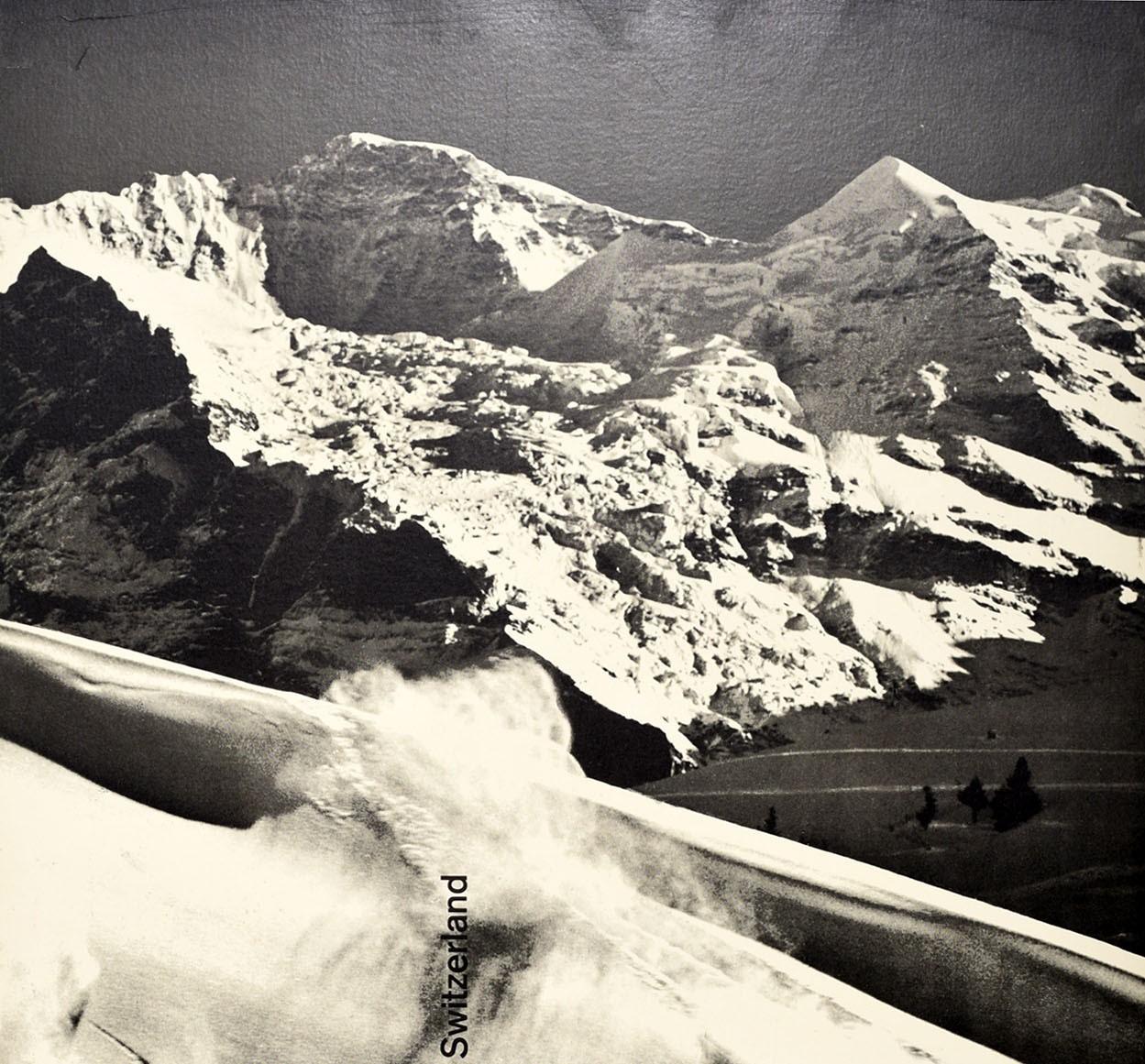 Original vintage ski travel poster for Wengen Berner Oberland Switzerland featuring a great black and white photo design showing skiers skiing at speed down a slope with snow topped mountain peaks in the distance, the title text running sideways in