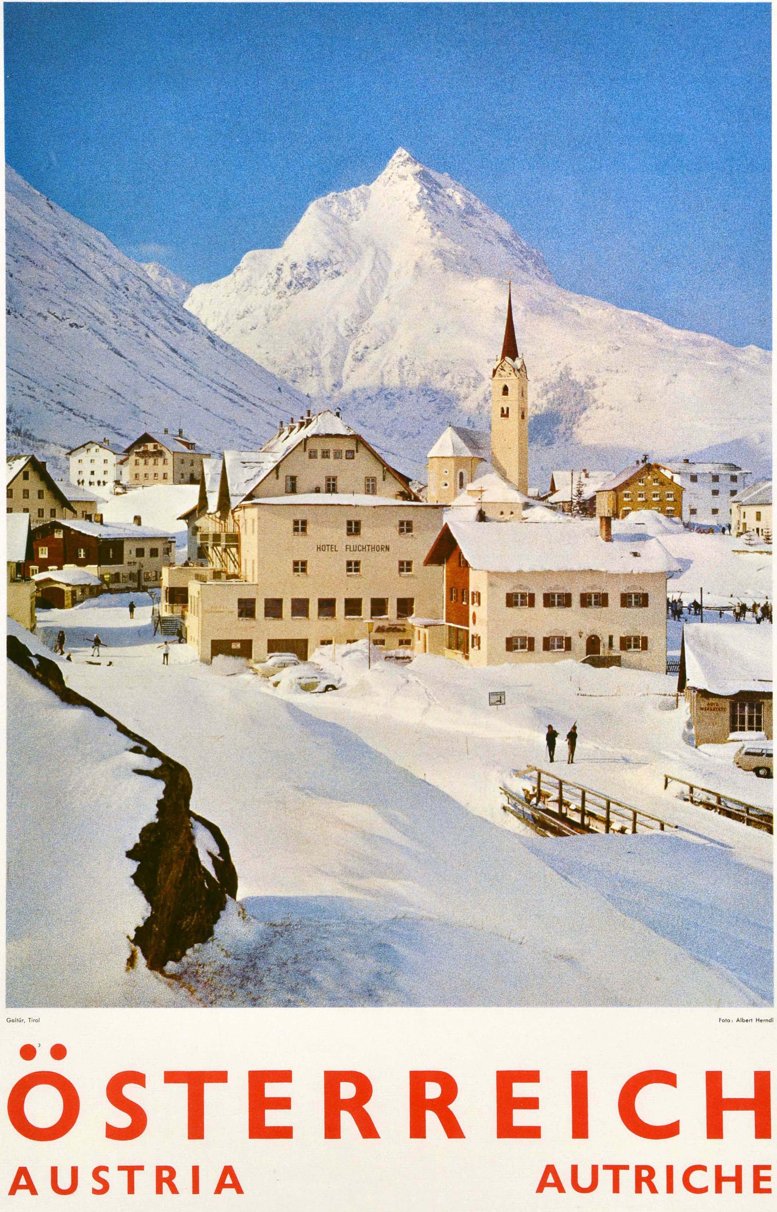 Original Winterreiseplakat für Österreich / Österreich / Österreich mit einer Fotografie der schneebedeckten Gebäude, darunter das Hotel Fluchthorn und ein Kirchturm im Skigebiet Dorf Galtur im oberen Paznauntal in Tirol / Tirol mit Menschen, die