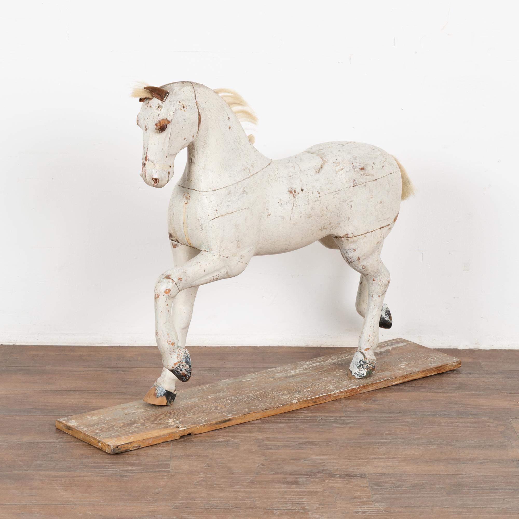 It is the very worn look that creates the wonderful appeal of this original painted and carved pine horse from Sweden. 
The white paint (and black hooves) has been worn and distressed to the pine below, while the tattered leather ears and horse hair