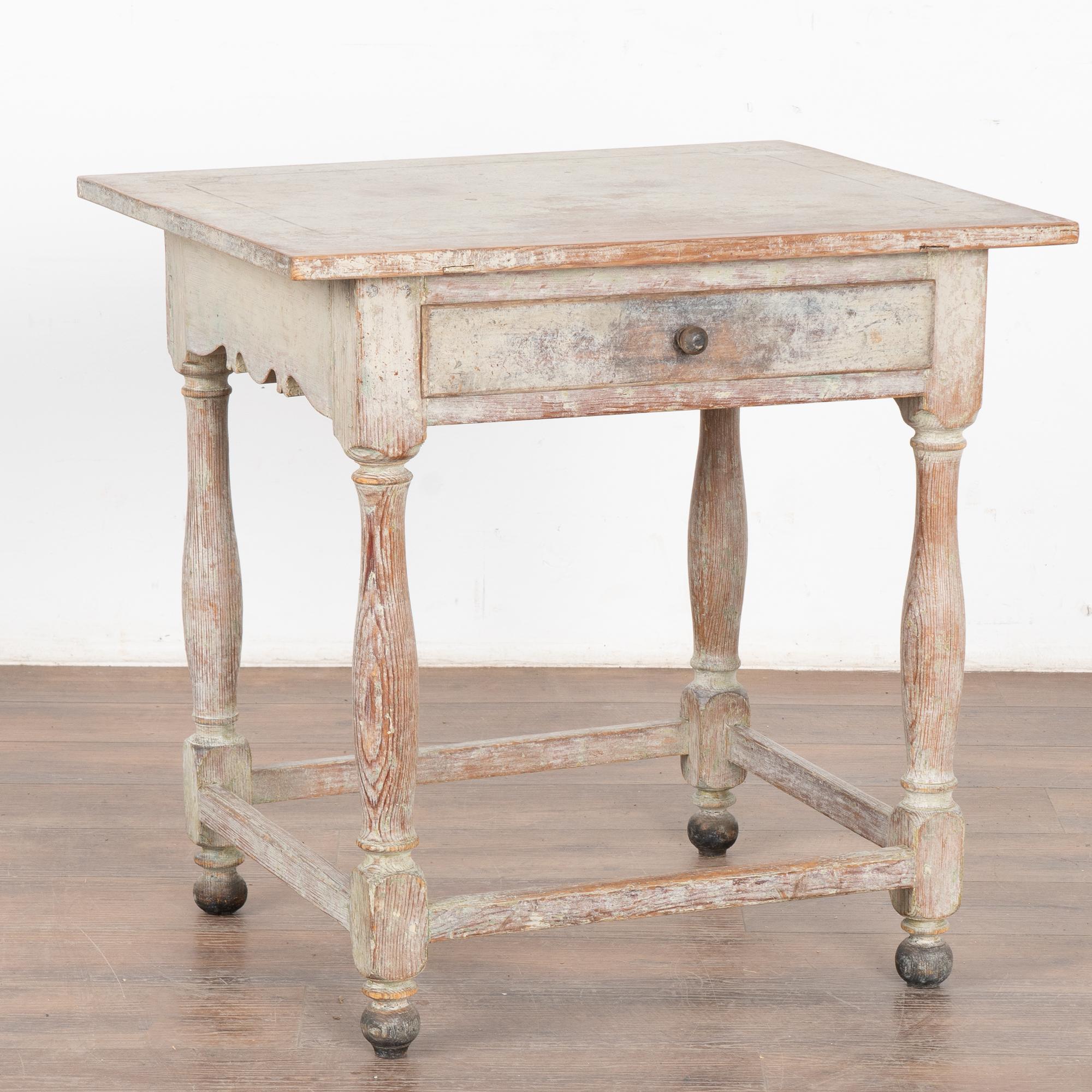 Table d'appoint originale en pin peint de style suédois avec pieds tournés, jupe sculptée et un seul tiroir. 
La peinture blanche d'origine a été usée jusqu'à la patine chaude du pin en dessous par des générations d'utilisation. Des vestiges d'une