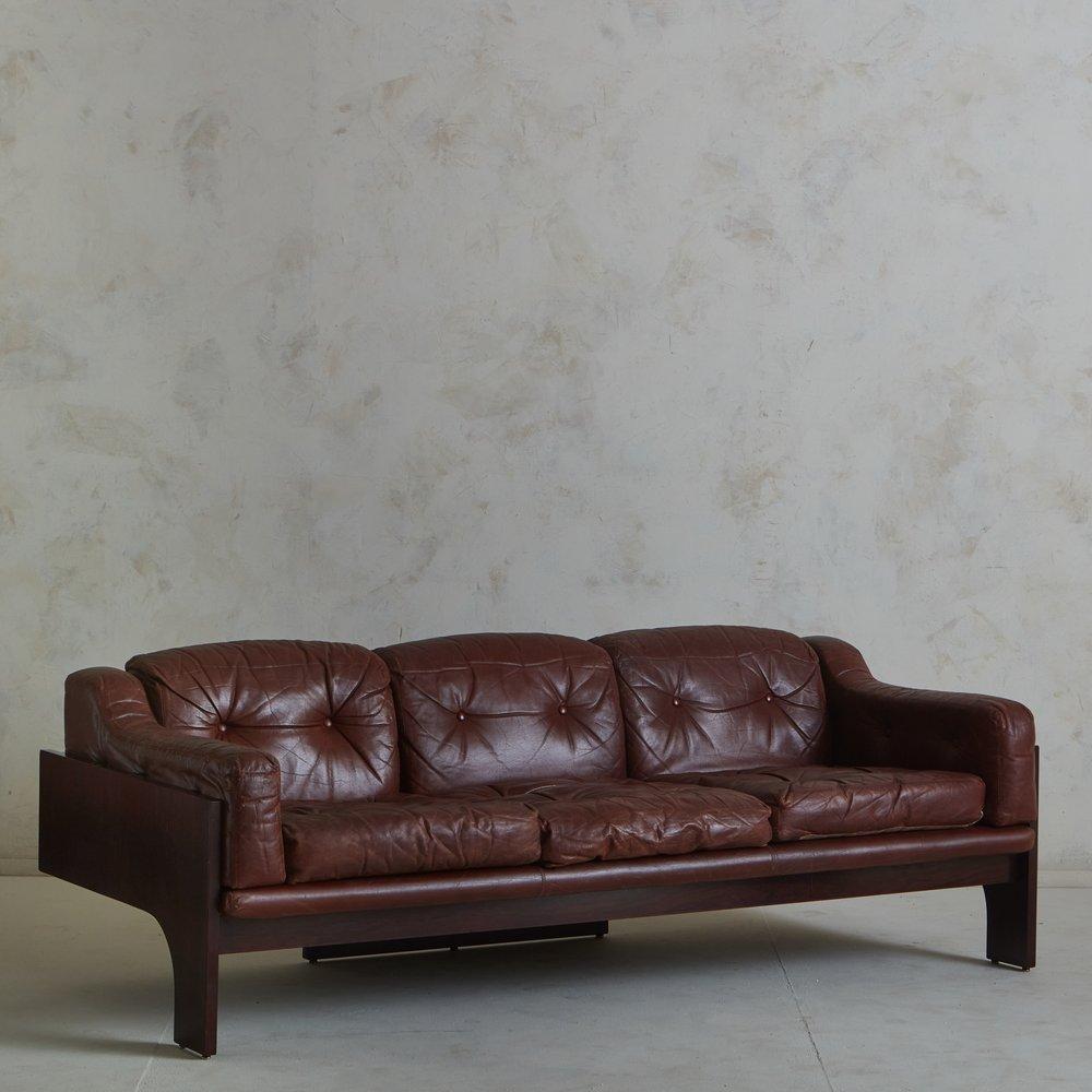 A 1960s Italian ‘Oriolo’ sofa designed by Claudio Salocchi for Sormani in the 1960s. This three-seat sofa has a sculptural rosewood frame with cutout details. It retains its original patinated leather upholstery with button tuft detailing. Unmarked.