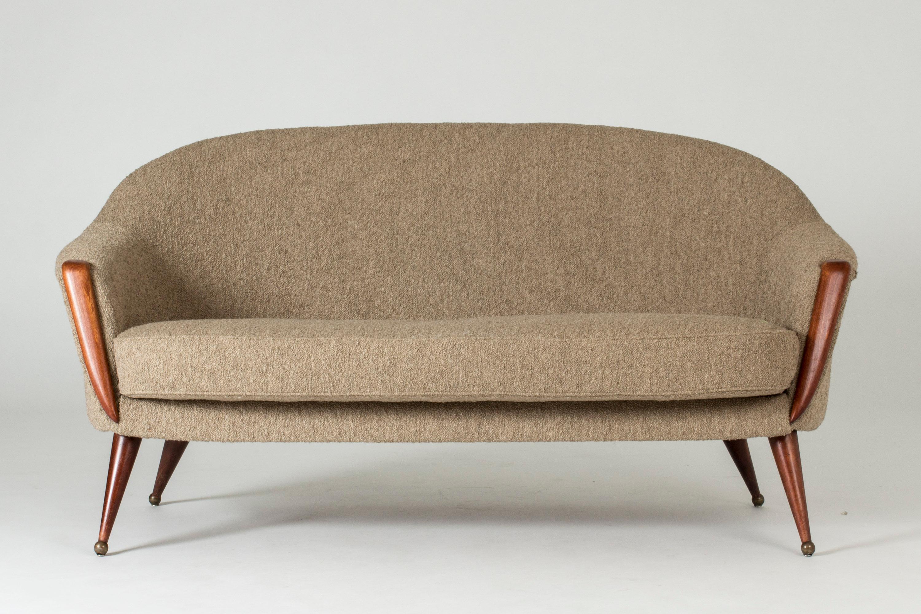 Elegant “Orion” sofa by Folke Jansson, in a rounded design. Brown wooden legs and details on the front, round brass ball feet. Bouclé upholstery.