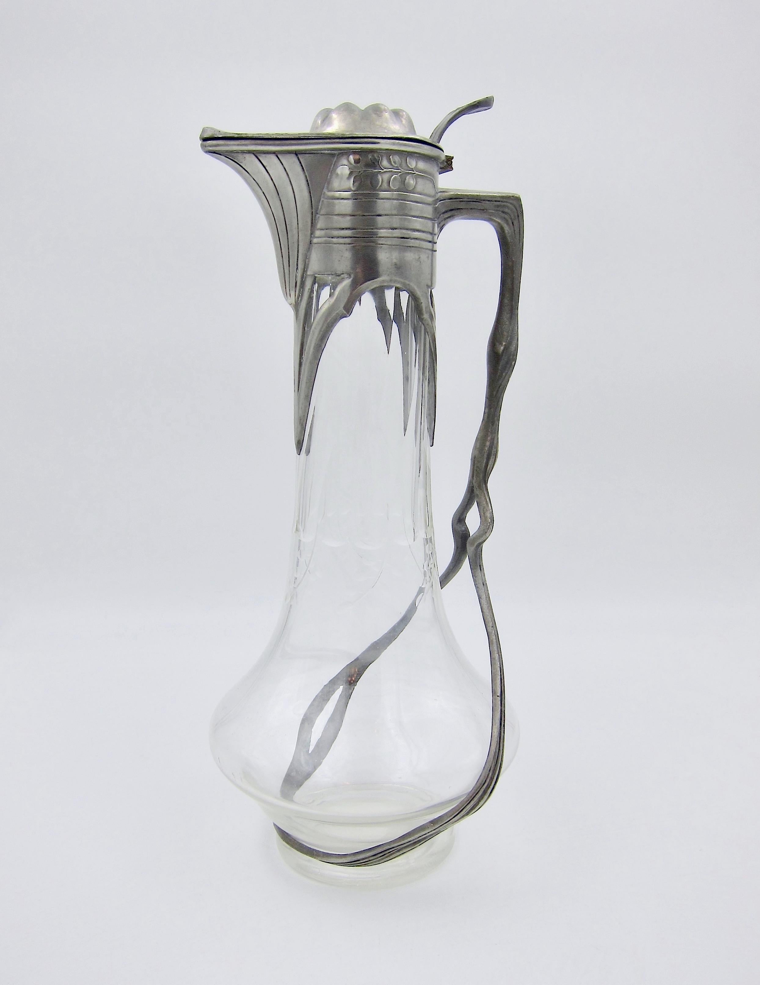 A German Jugendstil / Art Nouveau claret jug in clear glass with cut decoration in a silvery-gray pewter mount from Orivit AG of Cologne, circa 1900. The antique wine jug has a hinged and domed lid with strong linear patterns around the spout and