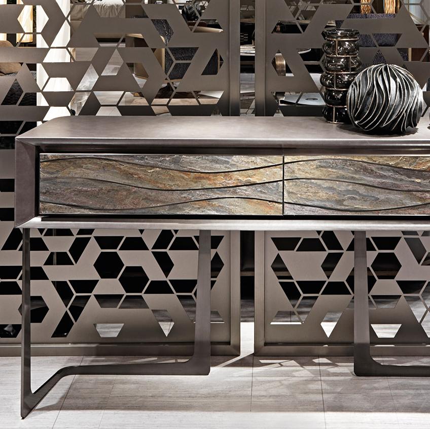 Console Table Orka with base structure in satinized stainless 
steel and with console table top's frame in wood covered with 
genuine leather in grey color. Top with 2 drawers with front in 
carved natural stone and with polished steel inserts.