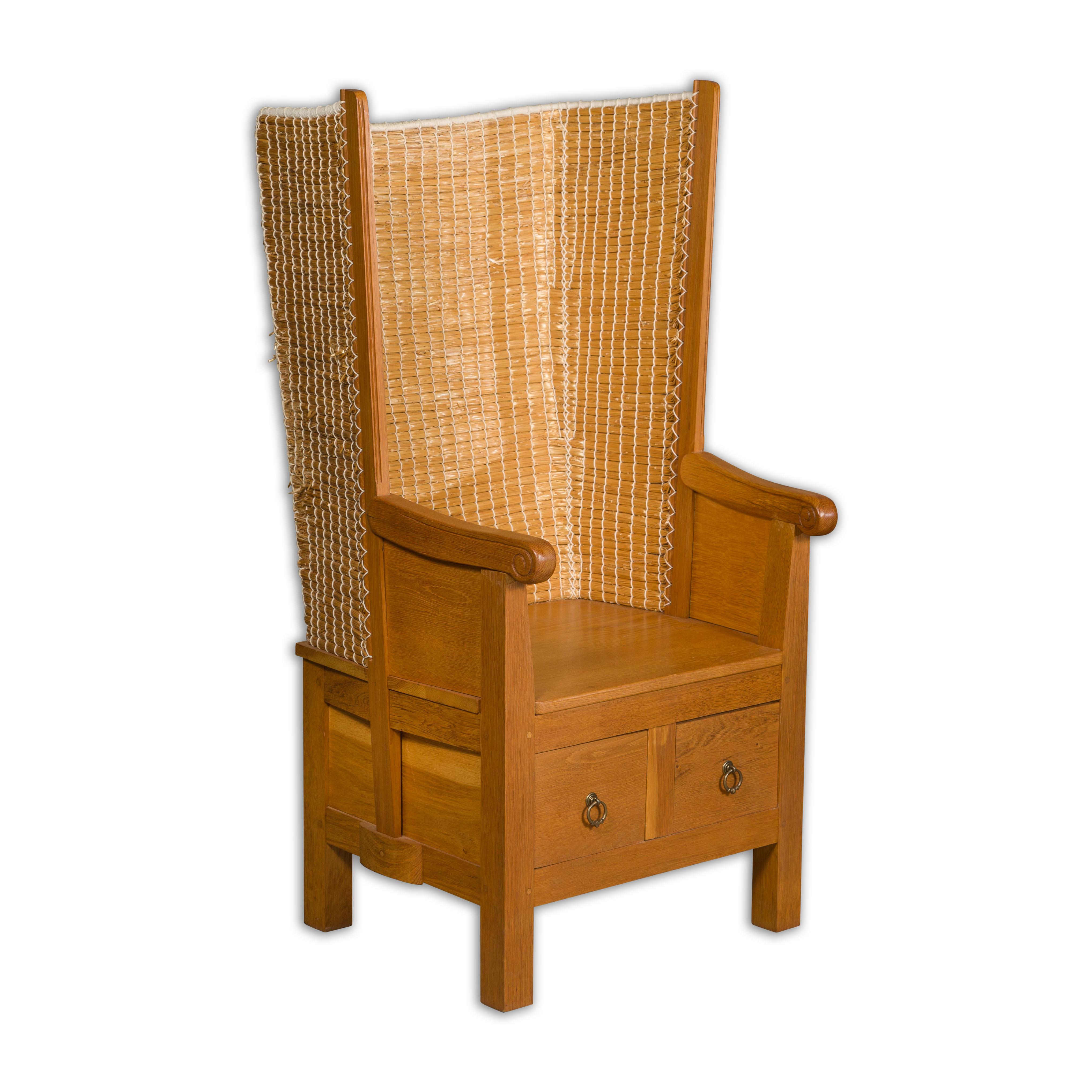 A vintage Scottish Orkney Island oak wingback chair with hand woven straw back, scrolling knuckles on the arms and two drawers in the lower section. A captivating vintage Scottish Orkney Island oak wingback chair from the mid 20th century, deftly