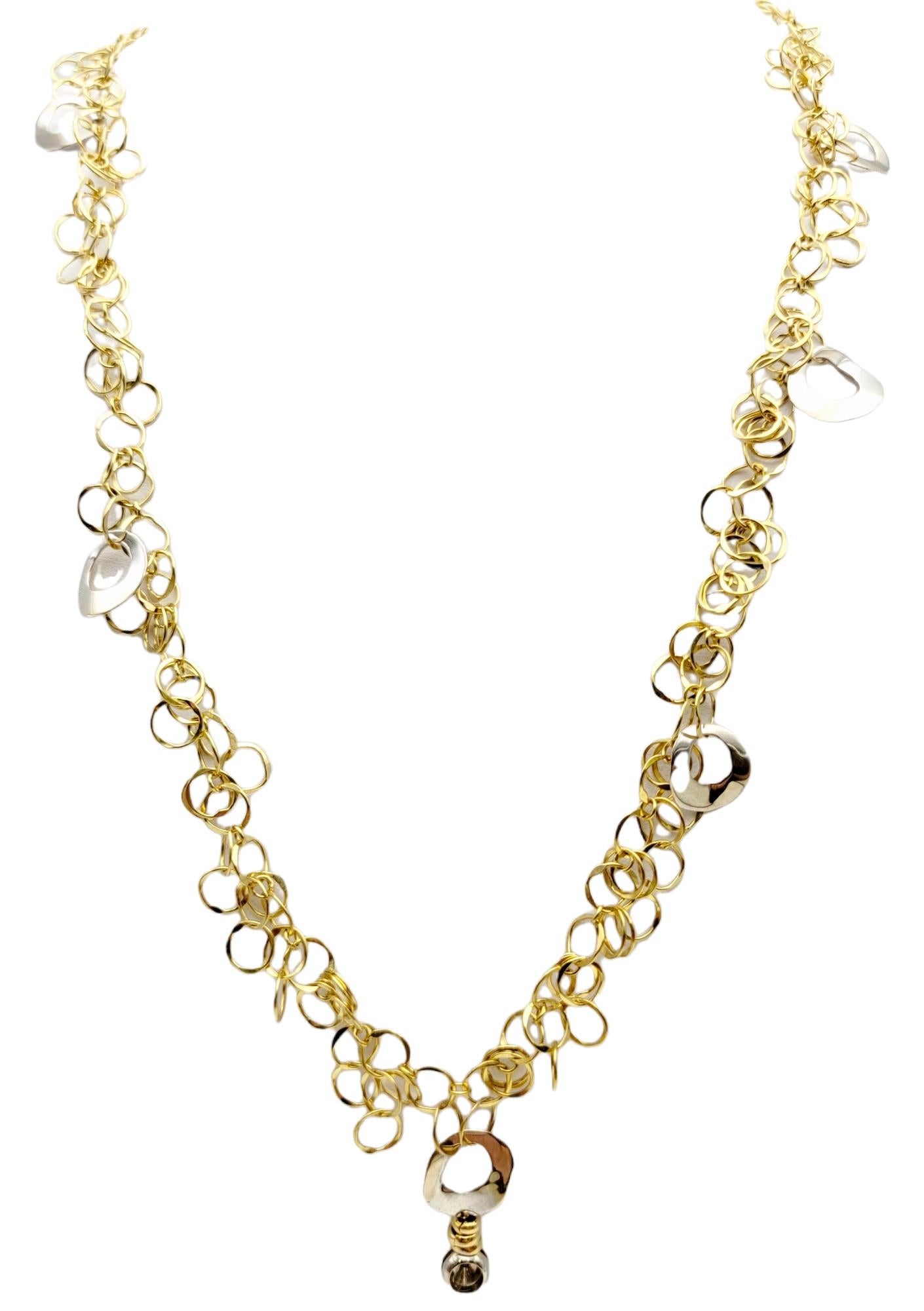 This beautiful necklace is a delicate masterpiece designed by Orlando Orlandini. It features a series of hammered yellow gold interlocking open circle links accented by a few larger white gold discs. Dangling off the center disc is a single bezel