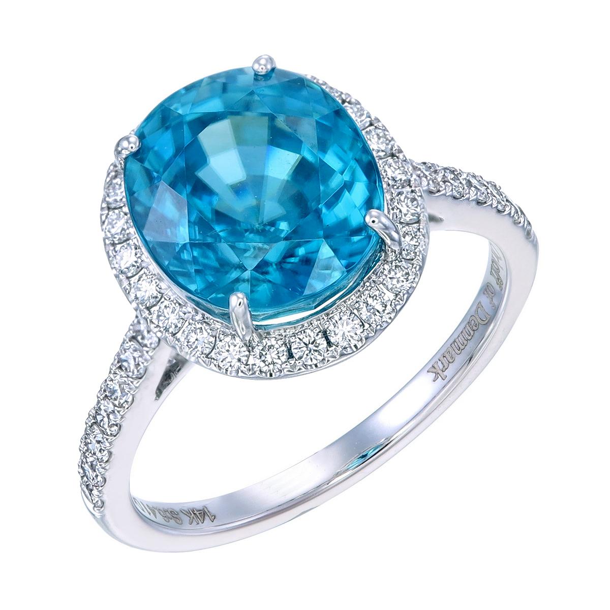 Natural Ocean Blue Zircon Engagement Ring.
This ring, which is set in 14 Karat white gold, features a 6.41 carat oval, natural sky blue zircon bolstered with SI1 diamonds encircling the gem,
extending halfway down the shank.
The combined glimmer of