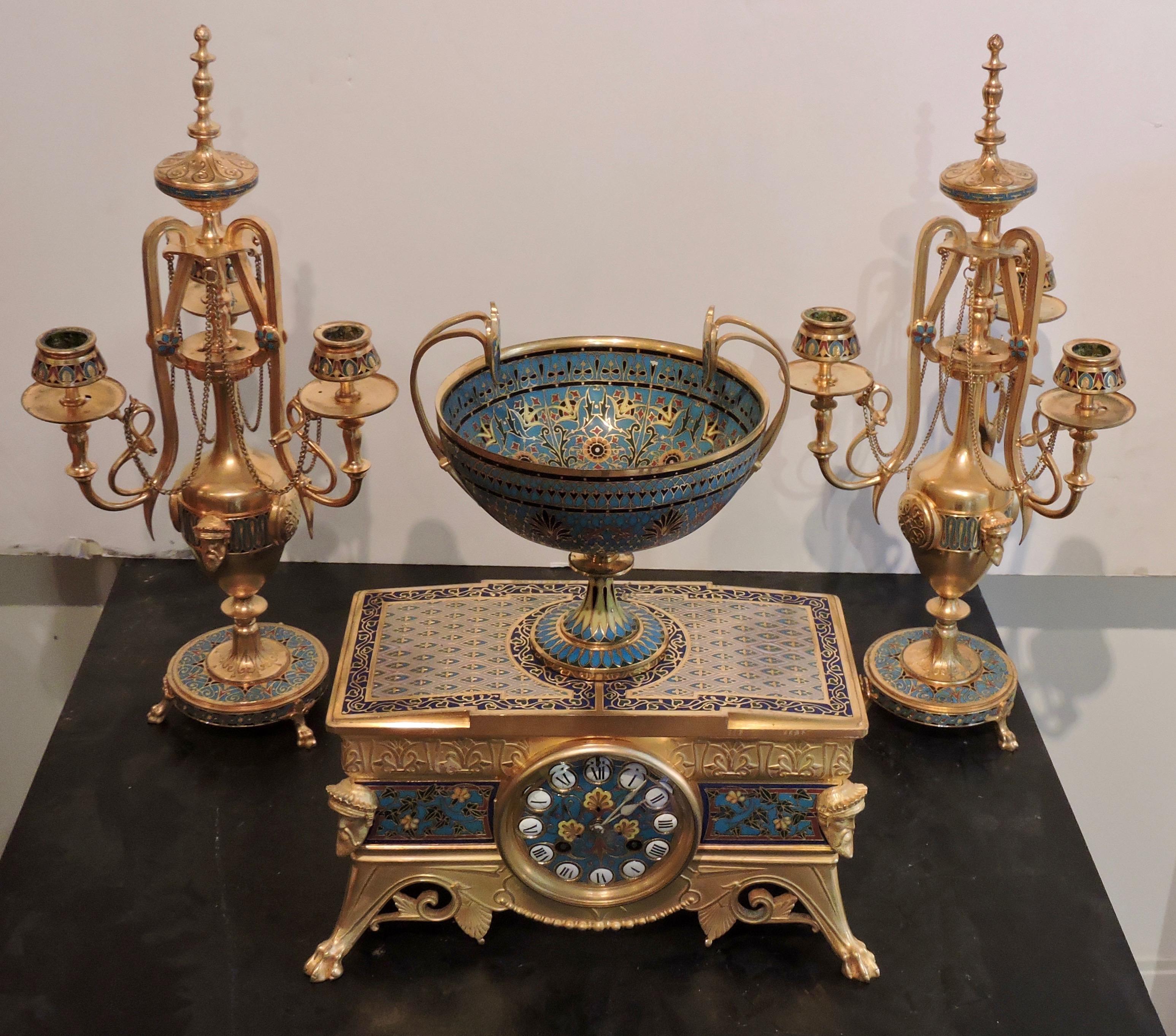 A French neo-Grec ormolu and champleve enamel garniture 
By Ferdinand Barbedienne, Paris, circa 1885 
Comprising a clock and a pair of three-branch candelabra, each piece decorated with trailing foliage and anthemia.
The clock surmounted by a