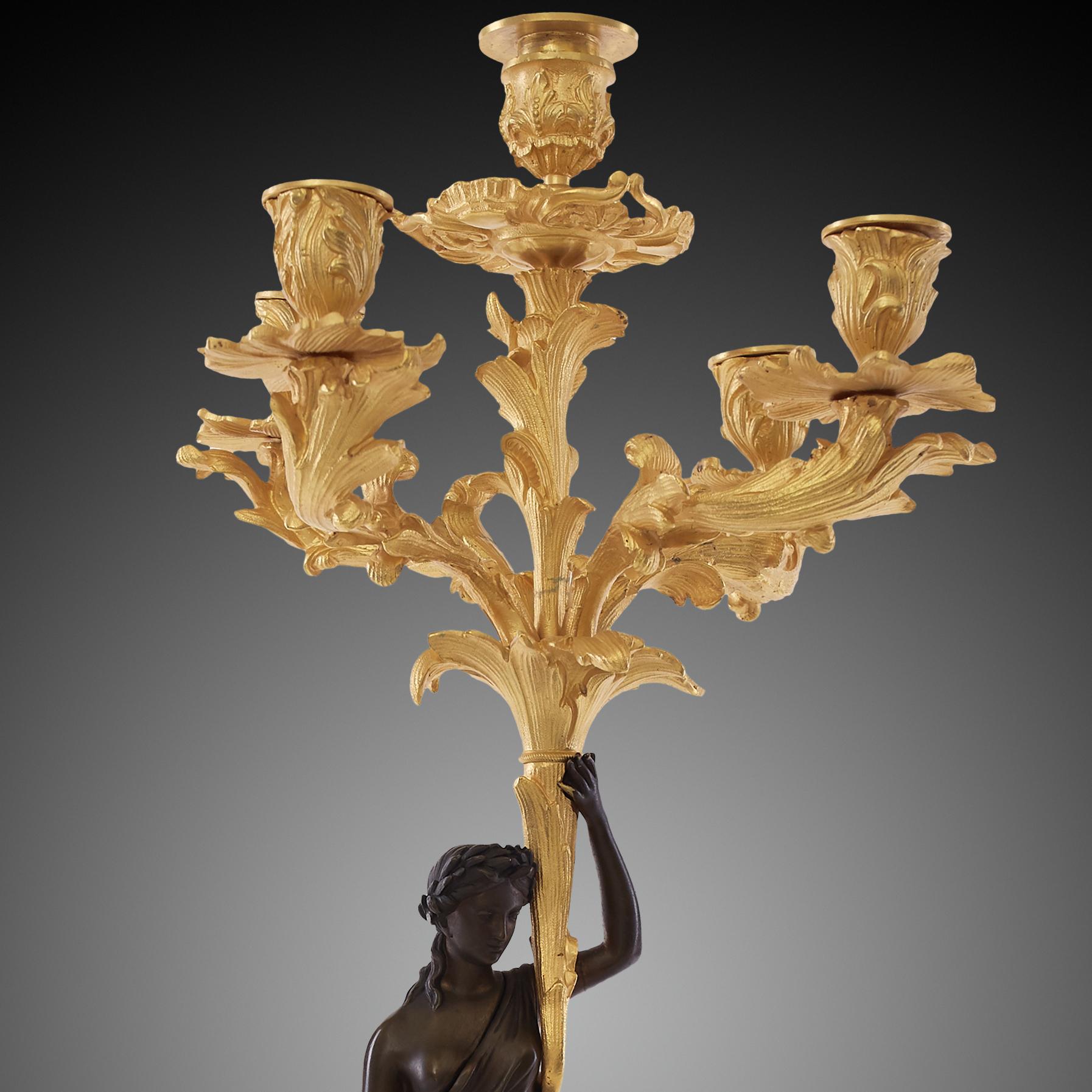 Es handelt sich um ein Paar vergoldeter Kandelaber, die vom Stil Ludwigs XVI. inspiriert sind - einem Stil, der seinen Ursprung in Frankreich hat. Der Hauptschaft der Kandelaber ist aus weiblichen Statuen gefertigt. Im Gegensatz zu den übrigen