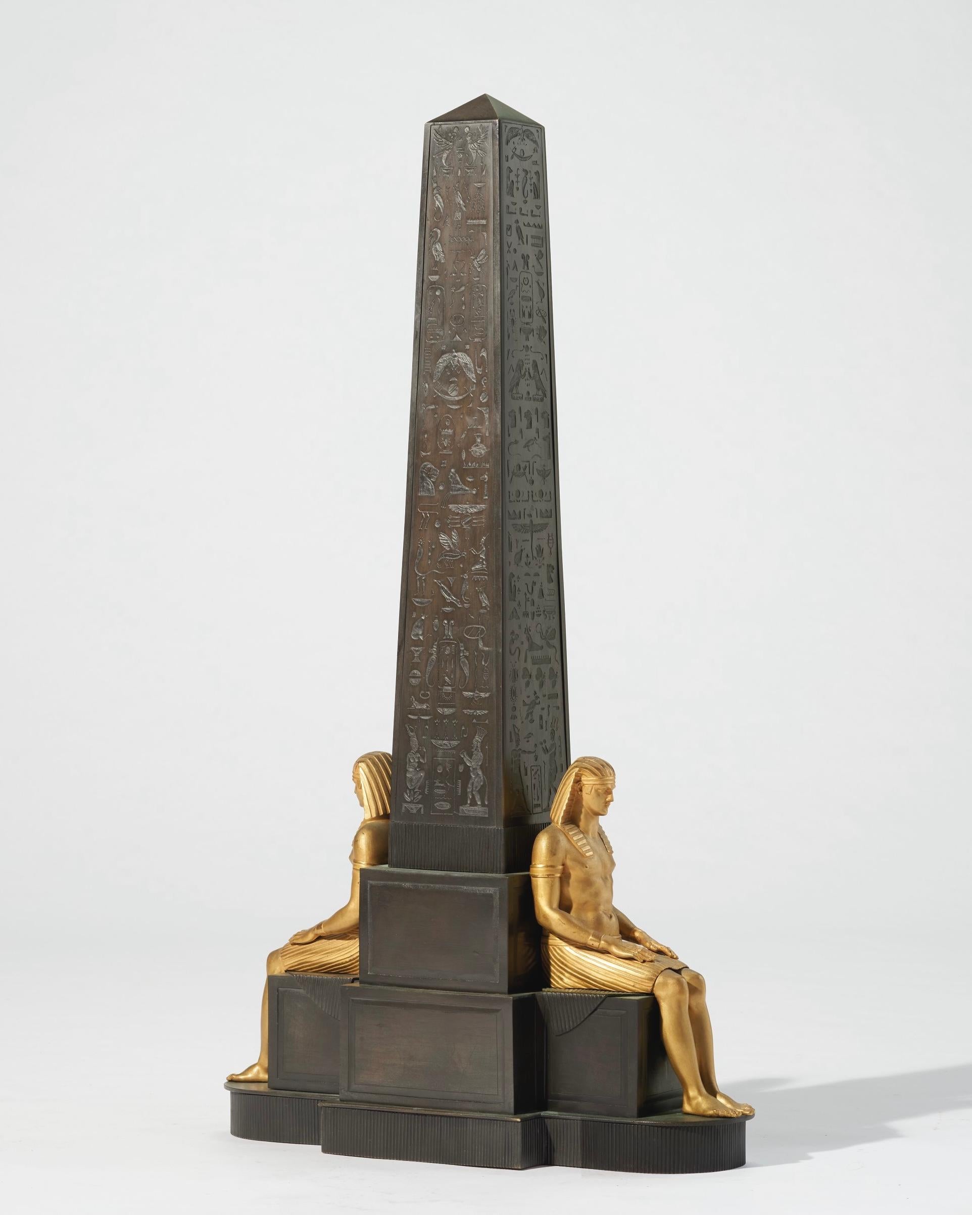 Our beautiful and very large French obelisk in the Empire style (35 3/4 in, 90.8 cm tall) with hieroglyphs and two seated gilt pharaohs dates from the mid nineteenth century.  It is apparently unsigned and in good condition.  From the collection of