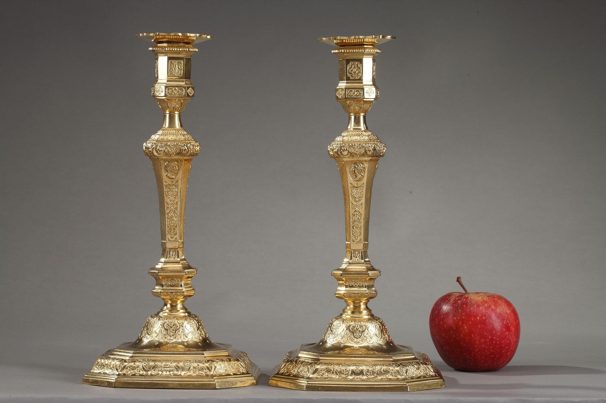 Pair of Louis XIV-Louis XV style candlesticks with chamfered angles. The stem of these ormolu Regency style lights is engraved with foliage, arabesques, antique vases and masks on a matting background. The stem presents several profiles in relief,
