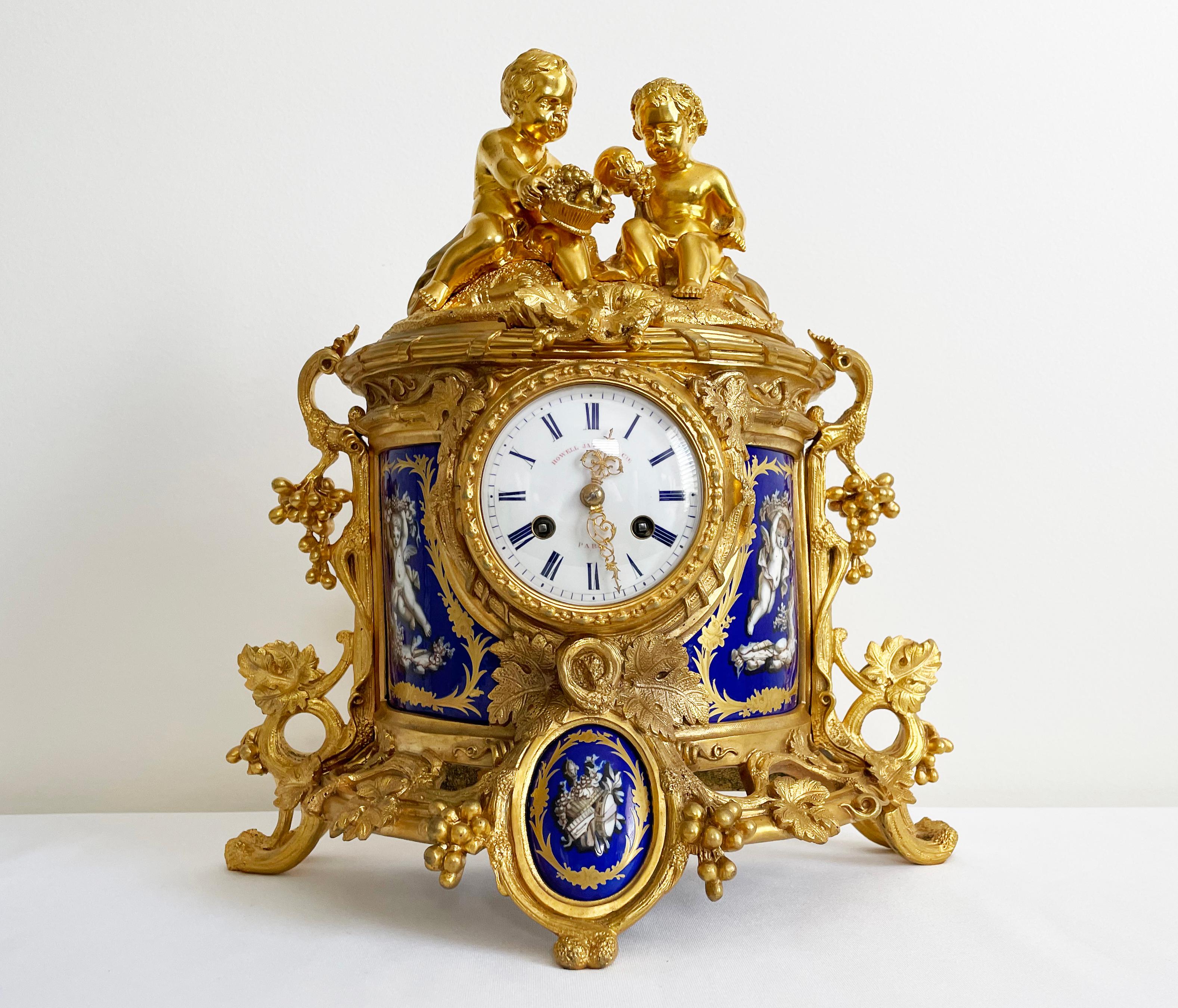 Vendue par Howell James and Co, cette belle horloge possède un boîtier en demilune doré décoré de moulures de vignes fruitières, les côtés avec des panneaux en céramique à fond bleu décorés de putti ailés, la base avec un cartouche central en