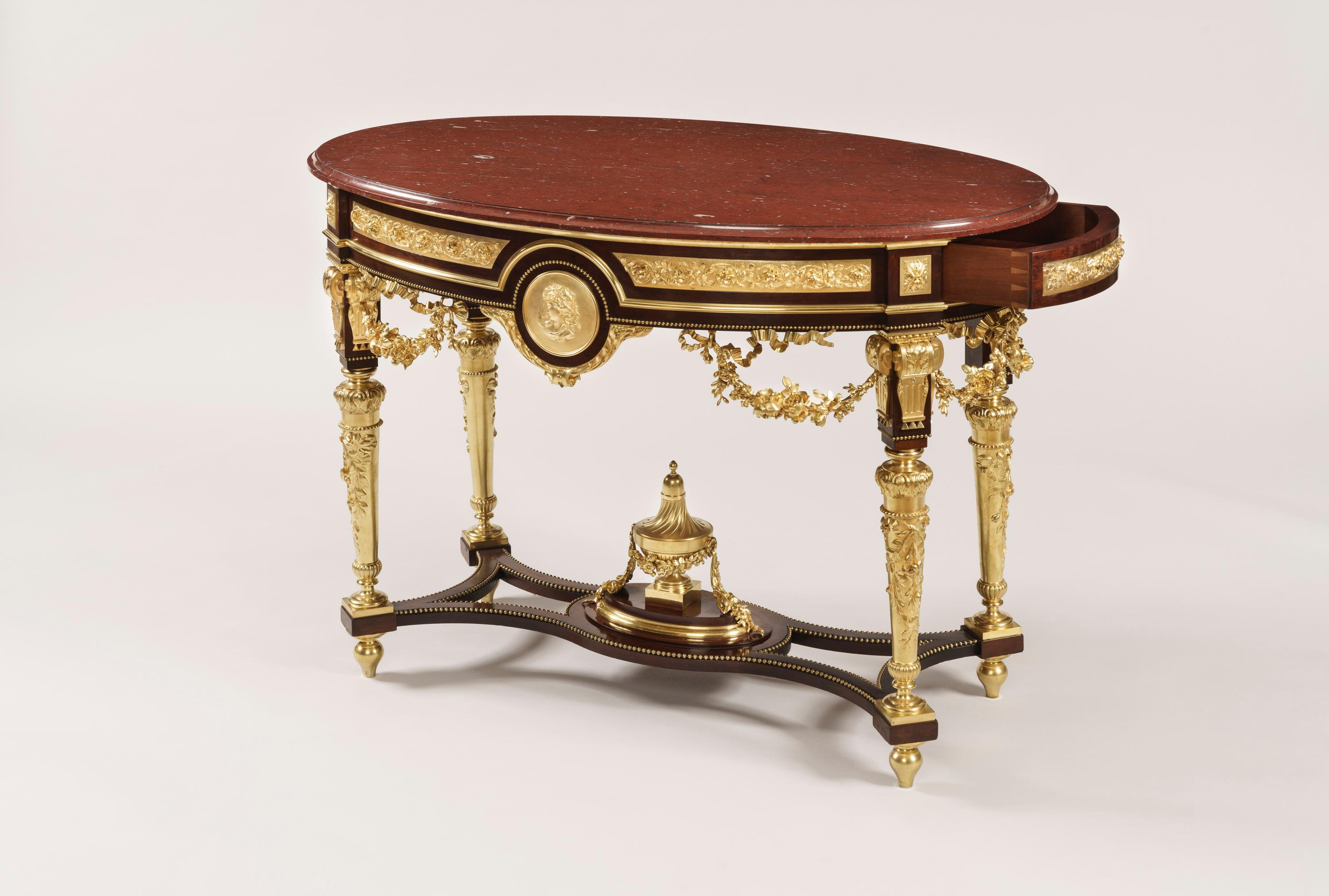 A superb centre table in the Louis XVI manner.

Of free standing elliptical form, the mahogany frame richly decorated with finely cast and chased ormolu, and having a thumbnail molded edge Griotte Pyrenean platform; rising from tapered ormolu