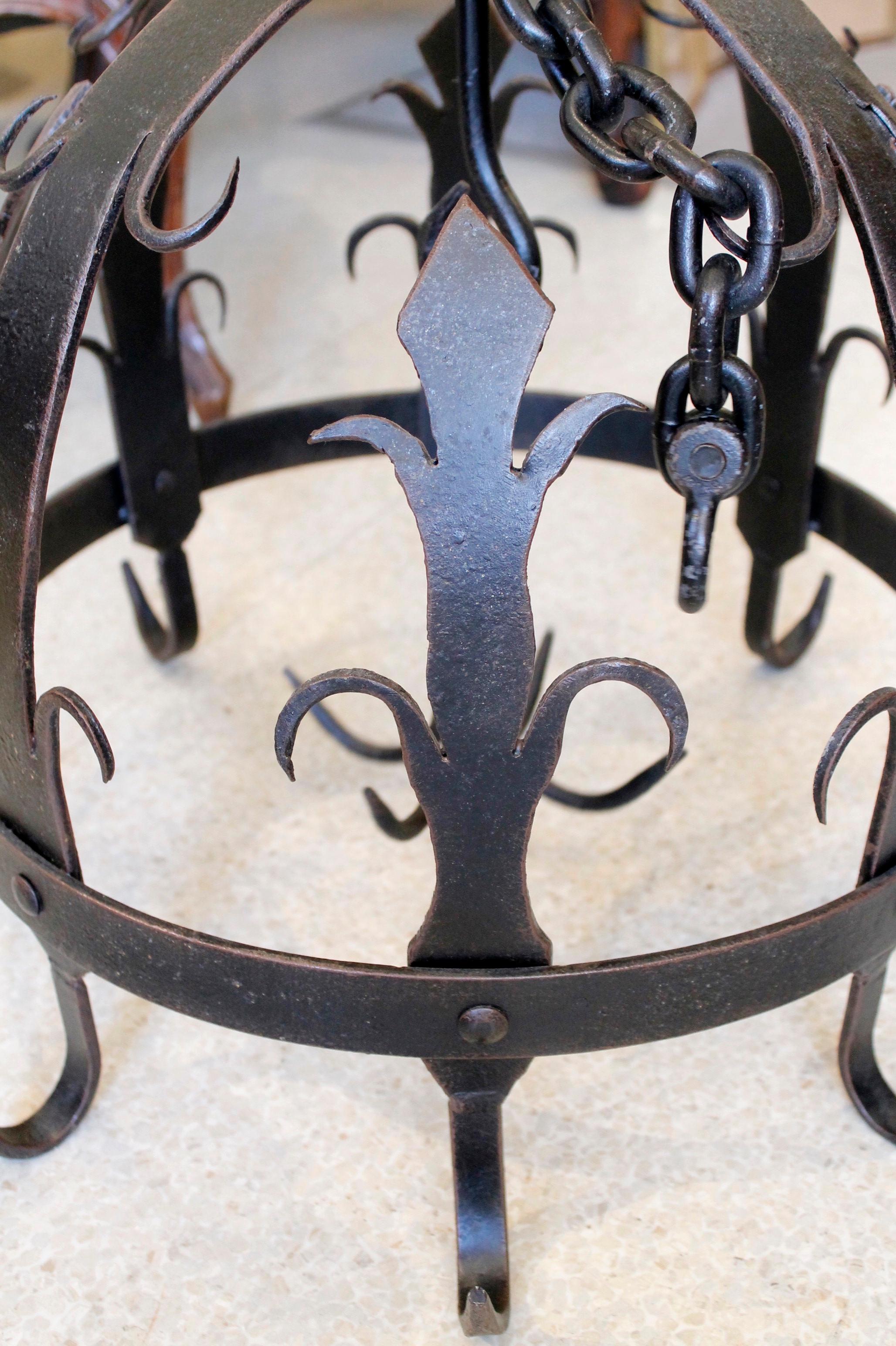 A sturdy half dome shaped pot rack of wrought iron, a Continental shape known as a 'Dutch crown,' featuring fleur-de-lys and scrolling decorative elements. 20th century. Very good condition, variations in patina. 

H: 26 adjustable with chain up to: