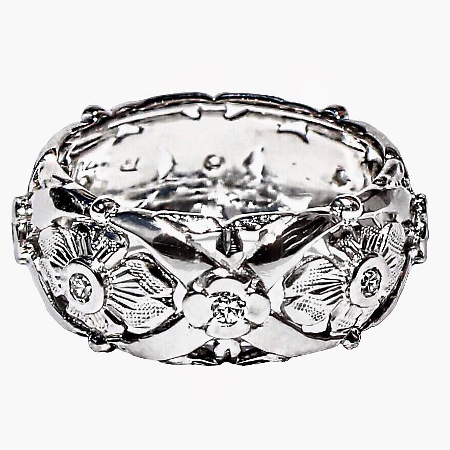This lovely and ornate Mid-20th Century 14K white gold wedding band, designed in a repeating floret motif, features flowers which are hand engraved and stippled. It is set with fine quality single cut diamonds at the center of each flower.  The