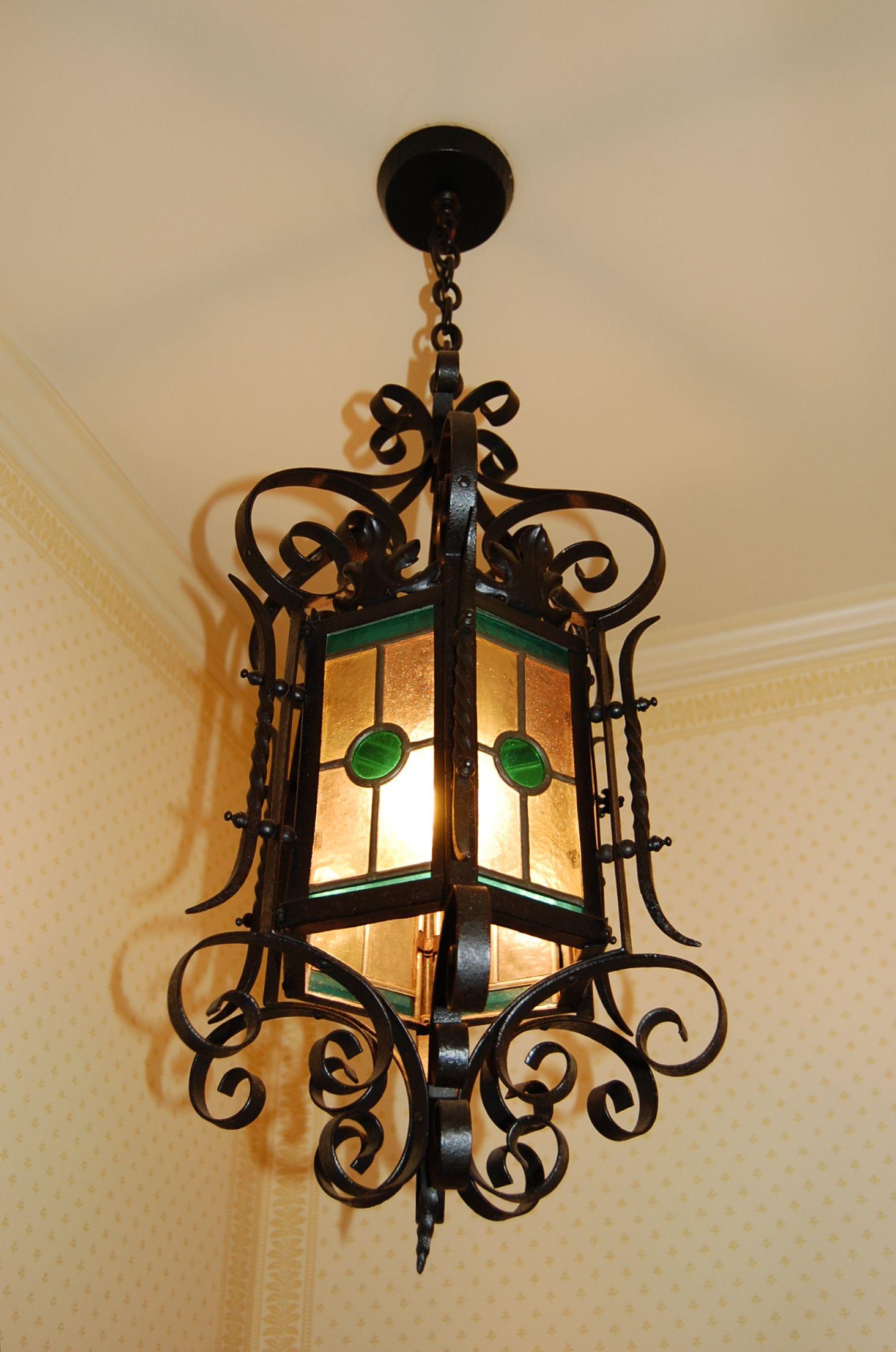 Hanging lantern with twisted iron details, scrolls and metal Acanthus leaf details. There are four panels of glass which include clear, aqua and a simulated Malachite glass center dot. The overall length including the chain is 40