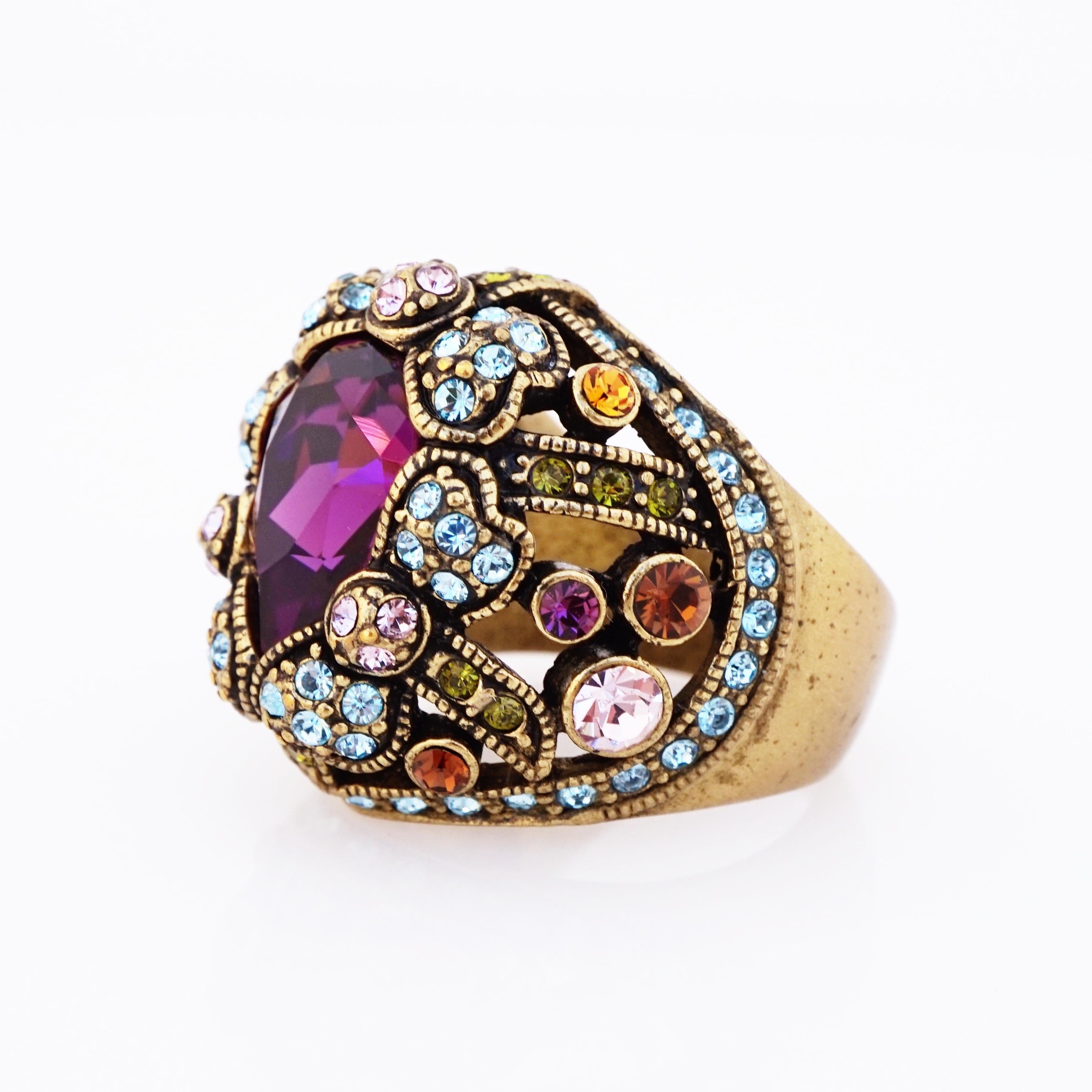 - Vintage item

- Collectible costume jewelry piece from the '90s

- Ring size 9.5 (US)

- Antique gold tone

- One large Amethyst-purple colored Swarovski crystal surrounded by multi-colored Swarovski crystal accents

- By Heidi Daus (signed on