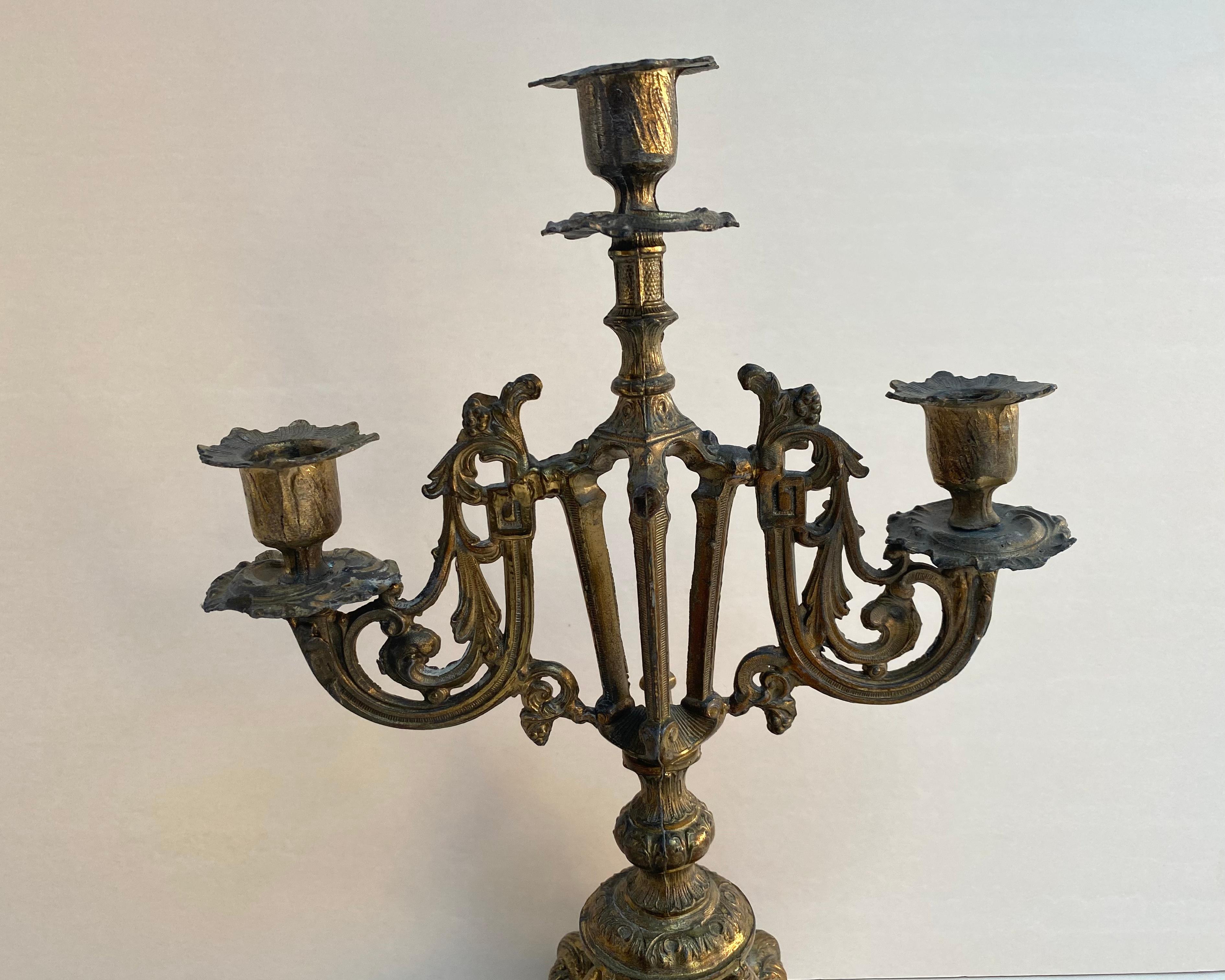 Antique brass candlestick/candelabra with 3 forged arms, Manufactured in France, 1900.

The base is very steady and can hold heavy candles. 

Metal candlesticks or candelabra in the modern world are used partly as home decor rather than for