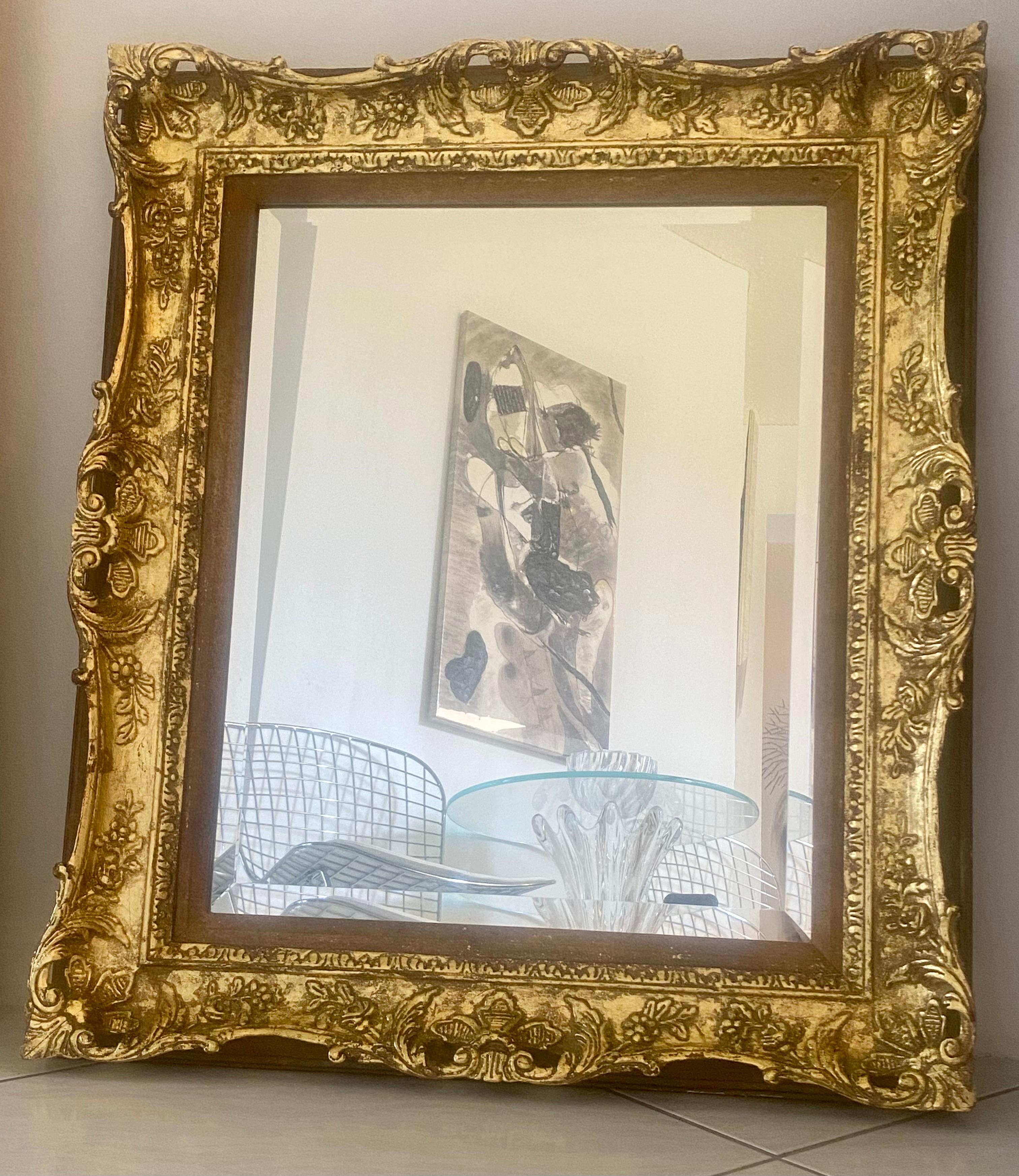 An ornately carved French antique frame with gold leaf and beveled mirror.