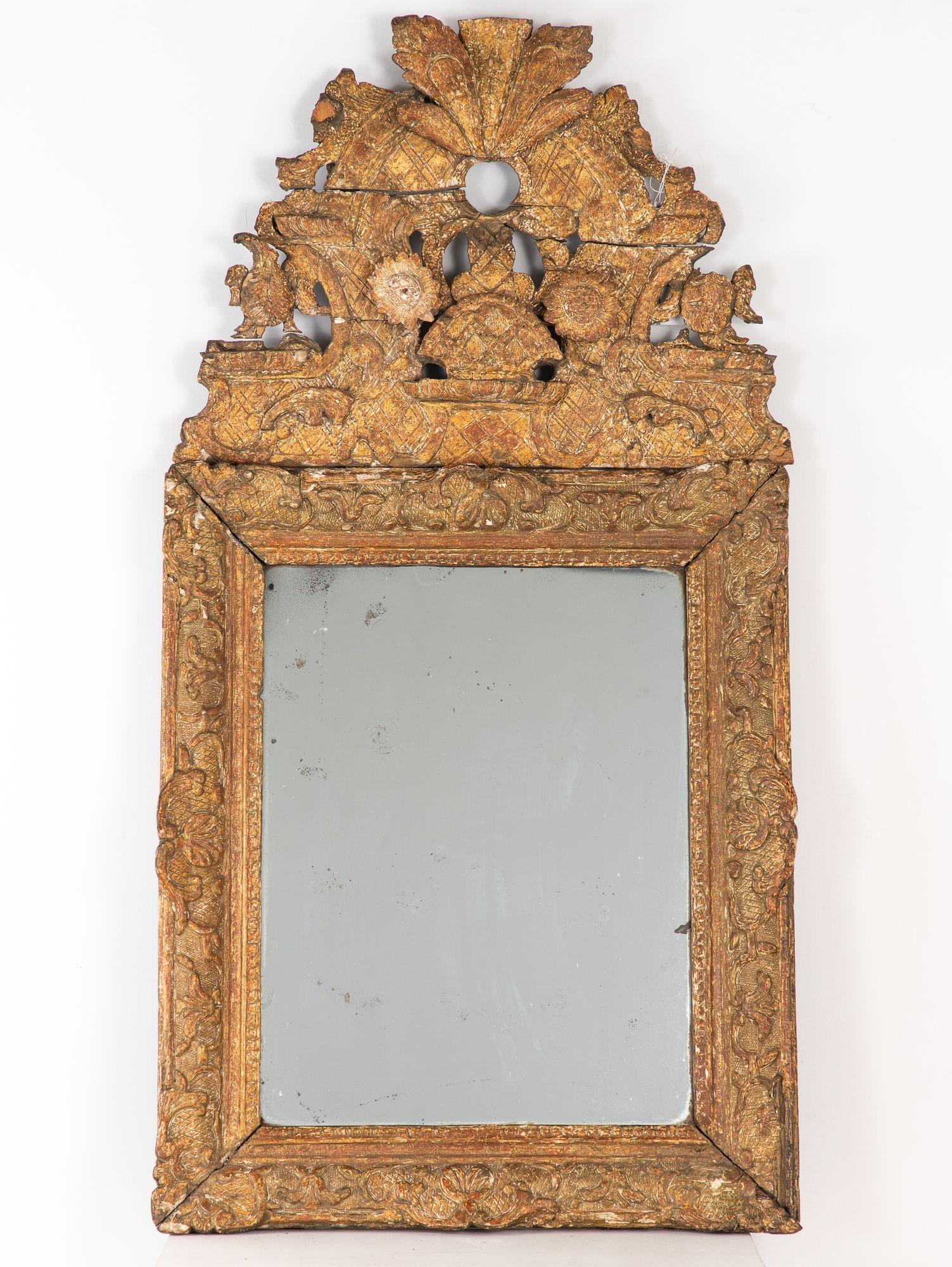 With its ornate crest of scrolls, rosettes, and birds, this intricately carved mirror exudes the elegance of 18th-century Swedish Baroque design. The giltwood frame, hand-carved and finished in layered gold leaf over gesso, shimmers with age and